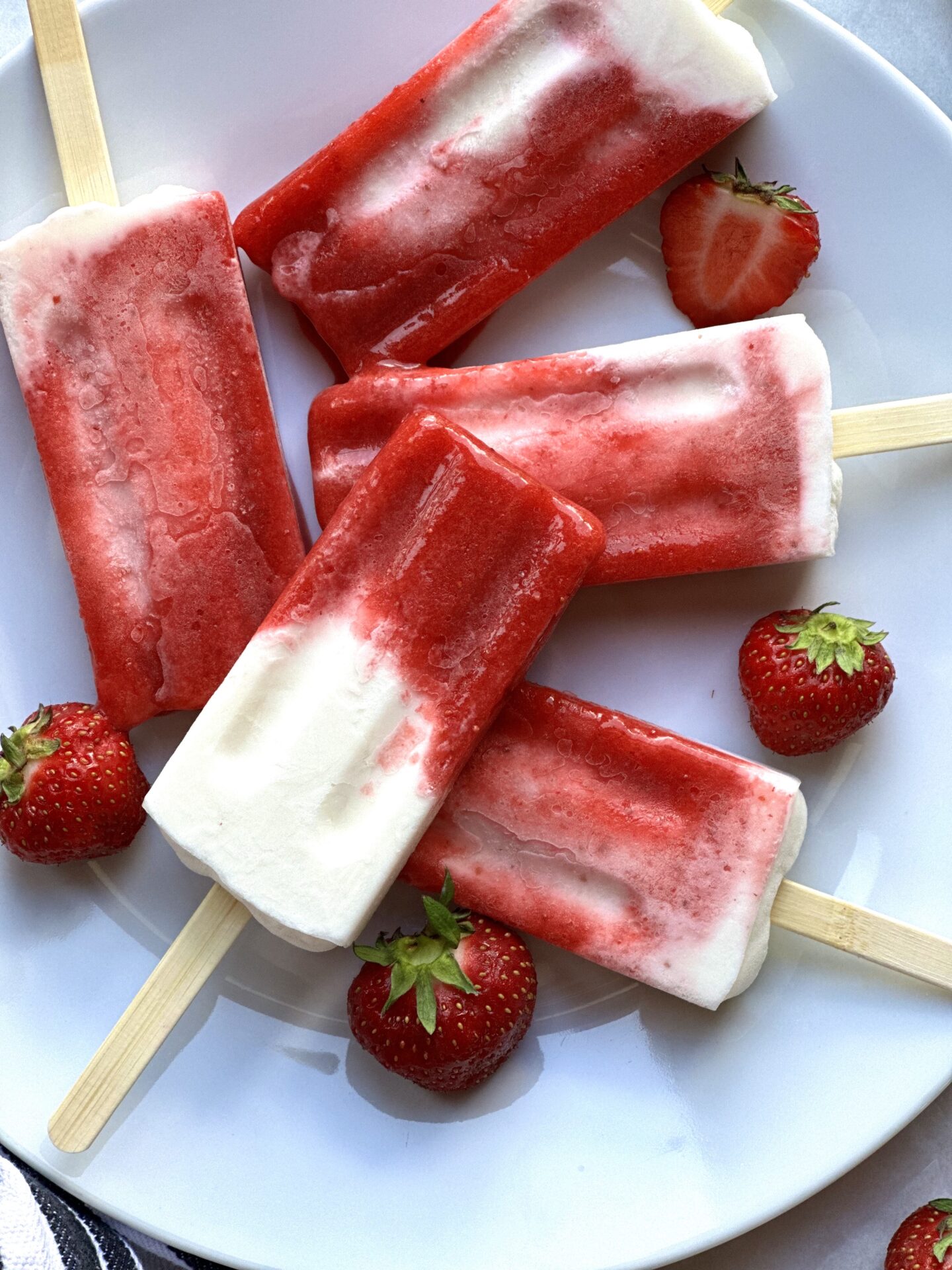 Plate of Strawberries and Cream breakfast popsicles surrounded by fresh strawberries