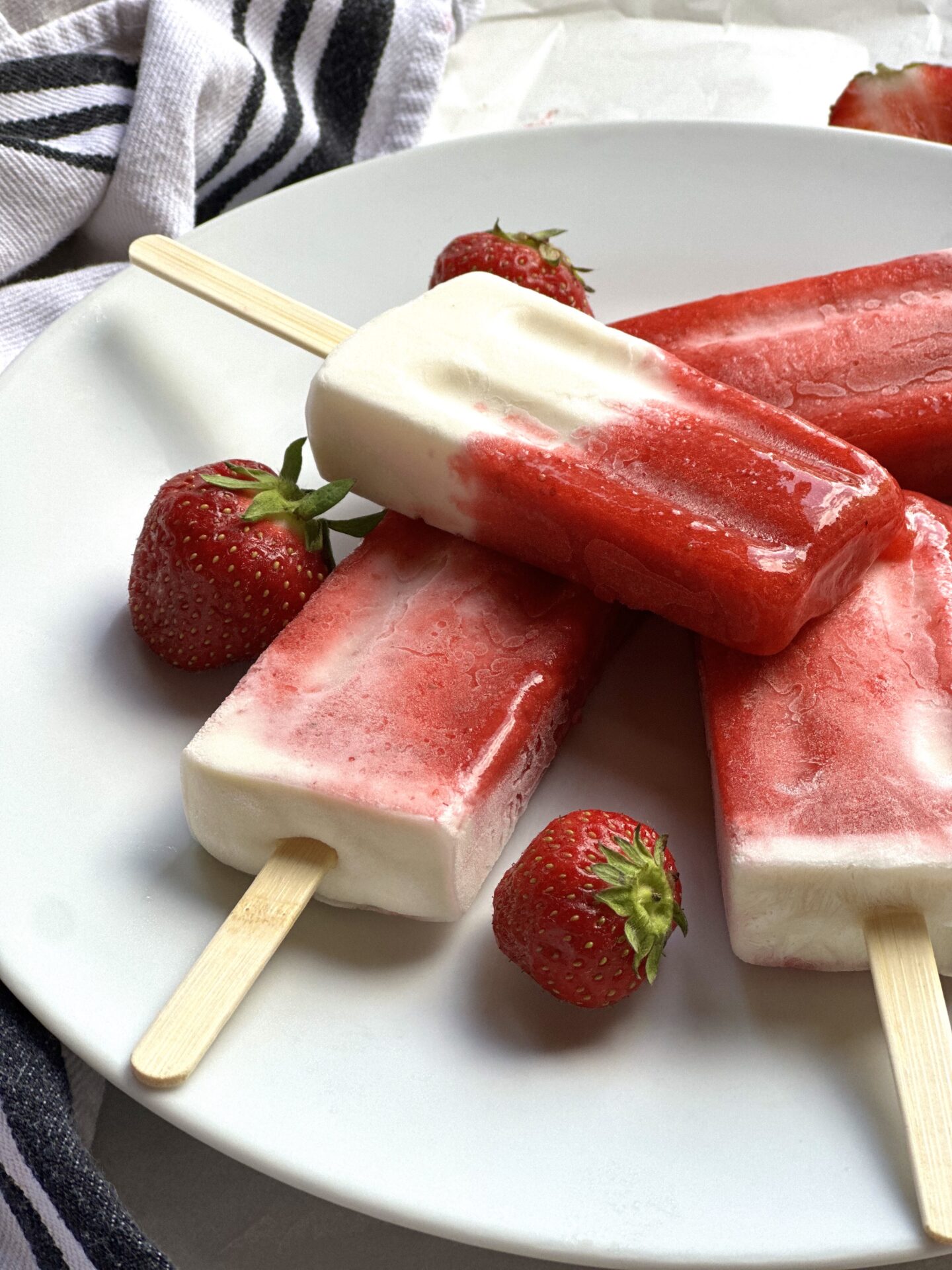 Plate of strawberries and cream breakfast popsicles seen from the side, surrounded by fresh strawberries