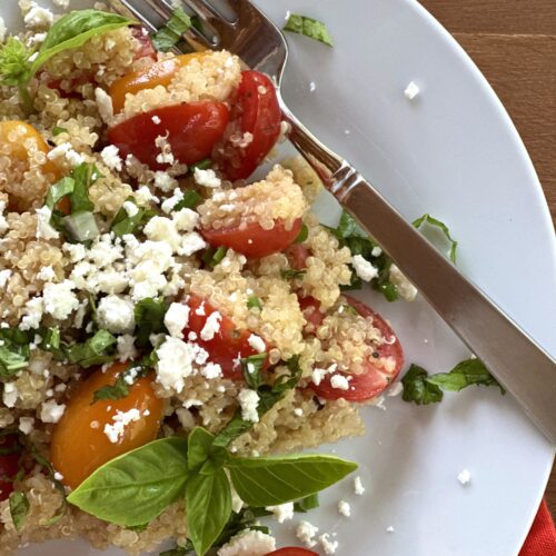 Cherry tomato and quinoa salad sprinkled with feta cheese and fresh herbs seen from above on a wood table