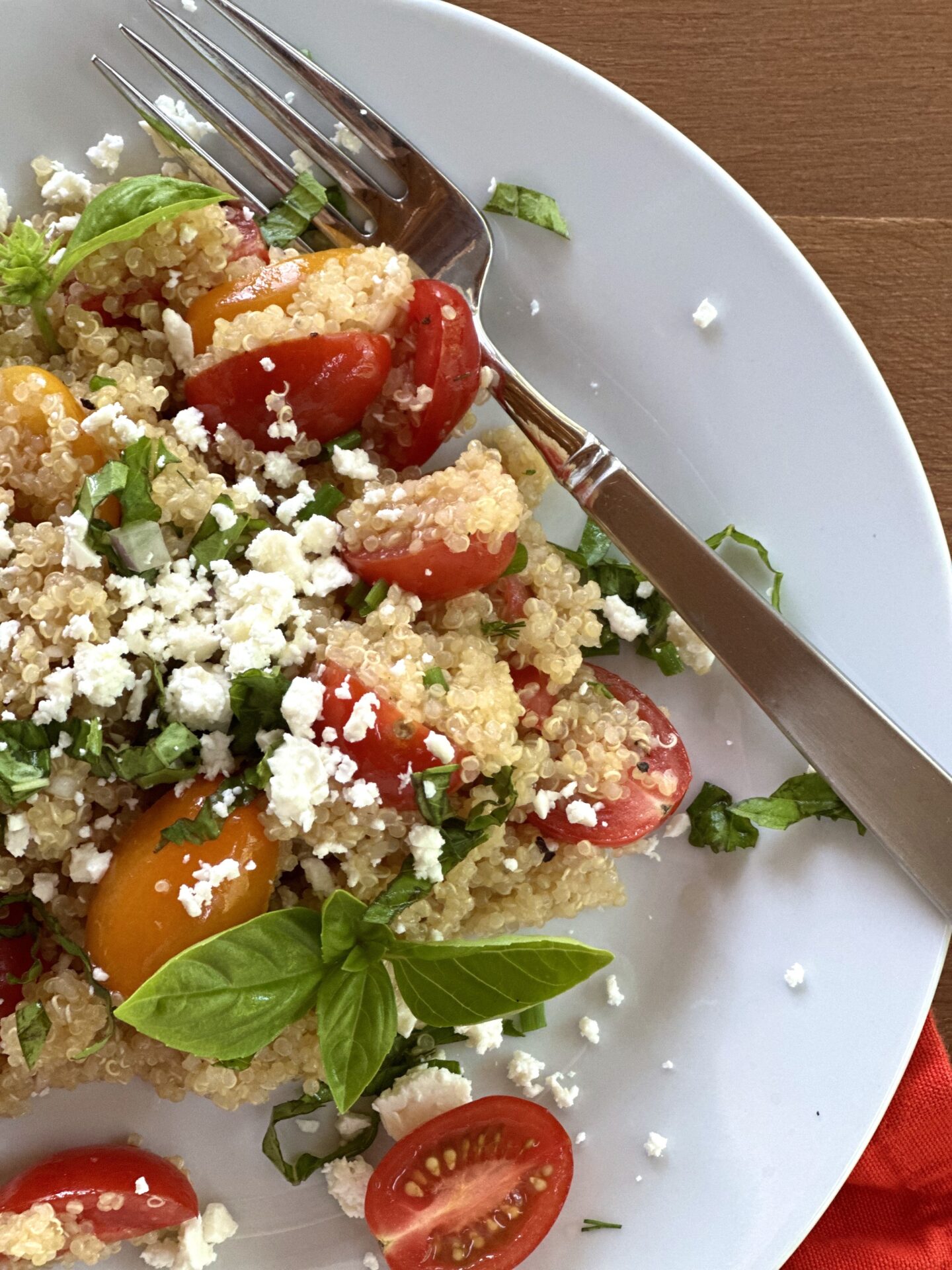 A close up image of cherry tomato quinoa salad garnished with crumbled feta cheese and fresh basil