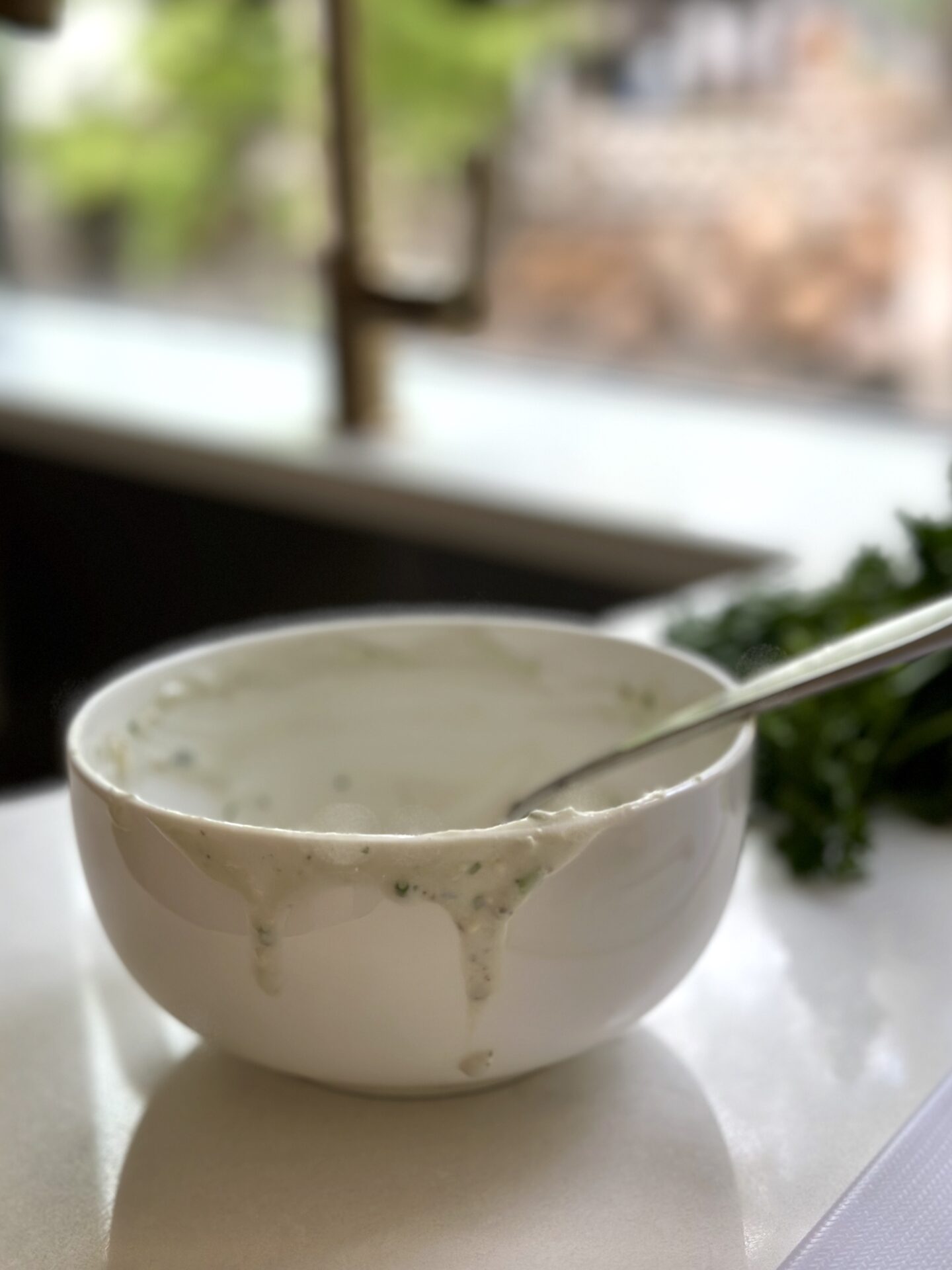 An empty bowl of homemade blue cheese dressing with drips coming down the side, sitting by a sink