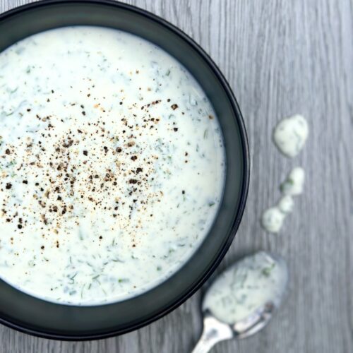 A bowl of creamy and fresh homemade buttermilk ranch dressing, with a spoon and drips of the dressing on a grey wood board