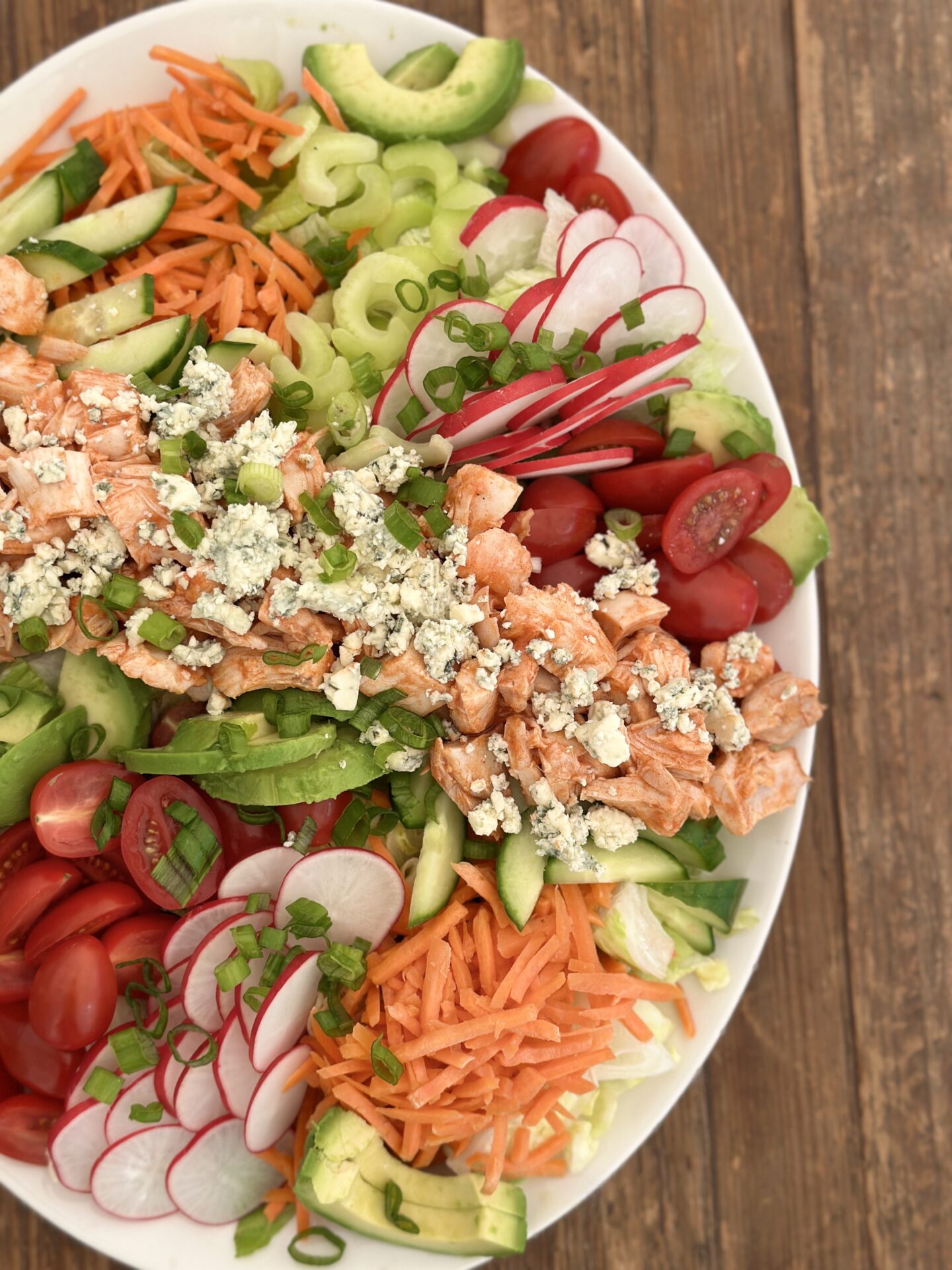 A large platter of Buffalo Chicken Dinner Salad full of bright fresh vegetables and big chunks of buffalo chicken is seen from above on a wood table