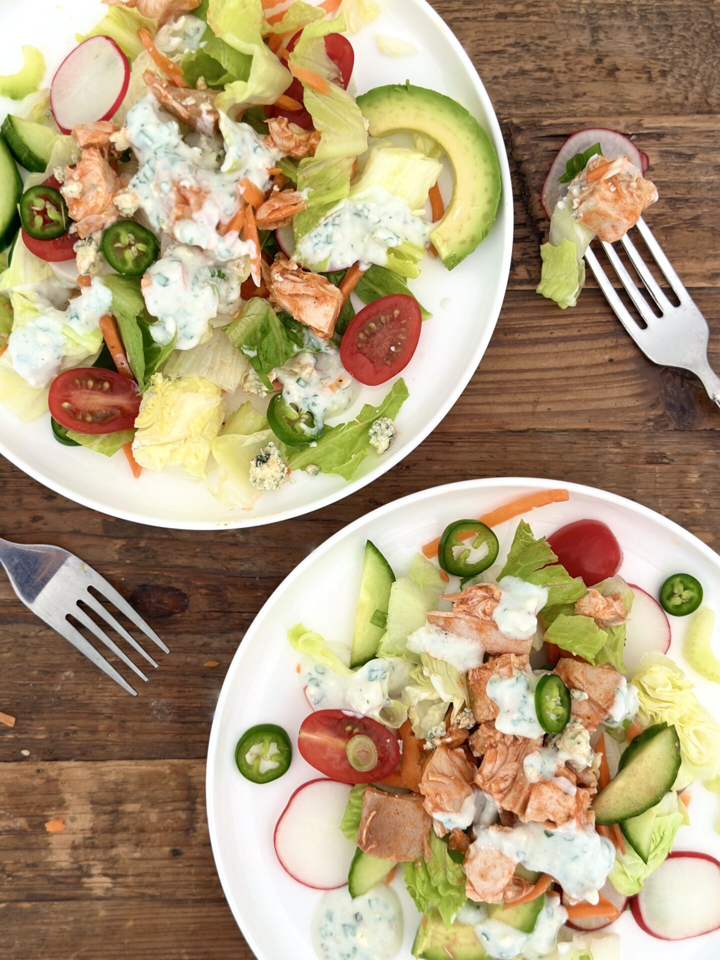 Two individual plates of Buffalo Chicken Dinner Salad are seen from above on a wood table with forks