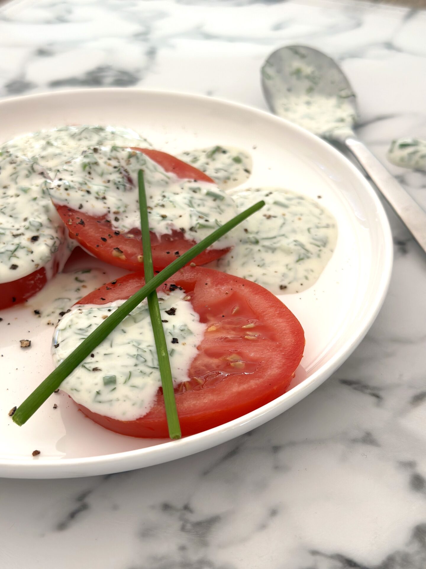 Plate of tomato slices with generous dollops of homemade buttermilk and herb ranch dressing