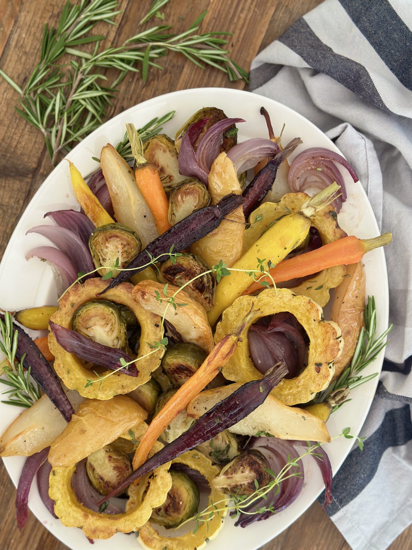 A platter of Maple Butter Roasted Vegetables with Pears is seen from above surrounded by fresh herbs