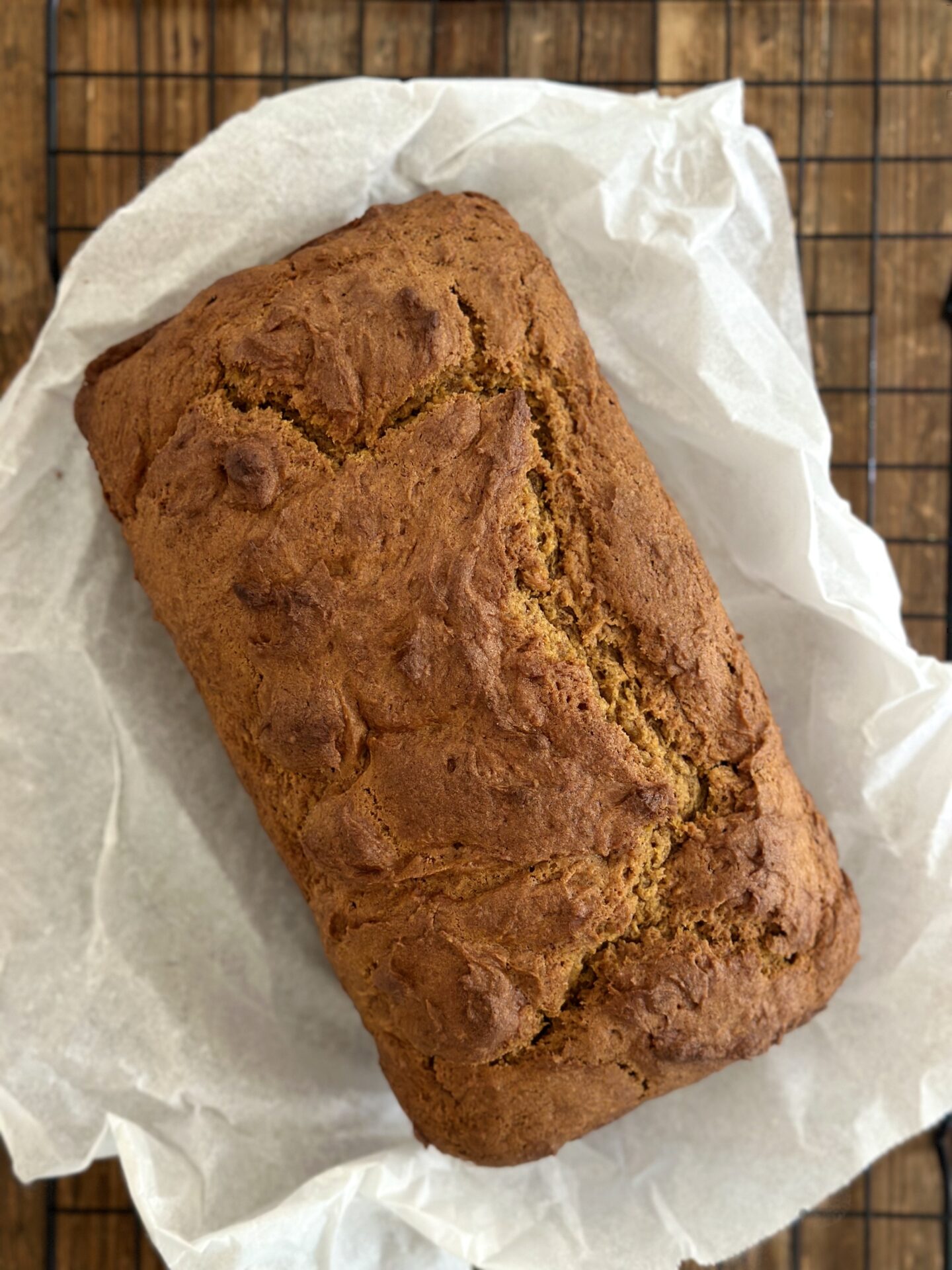 A golden loaf of pumpkin bread fresh from the oven is cooling on a parchment paper lined rack