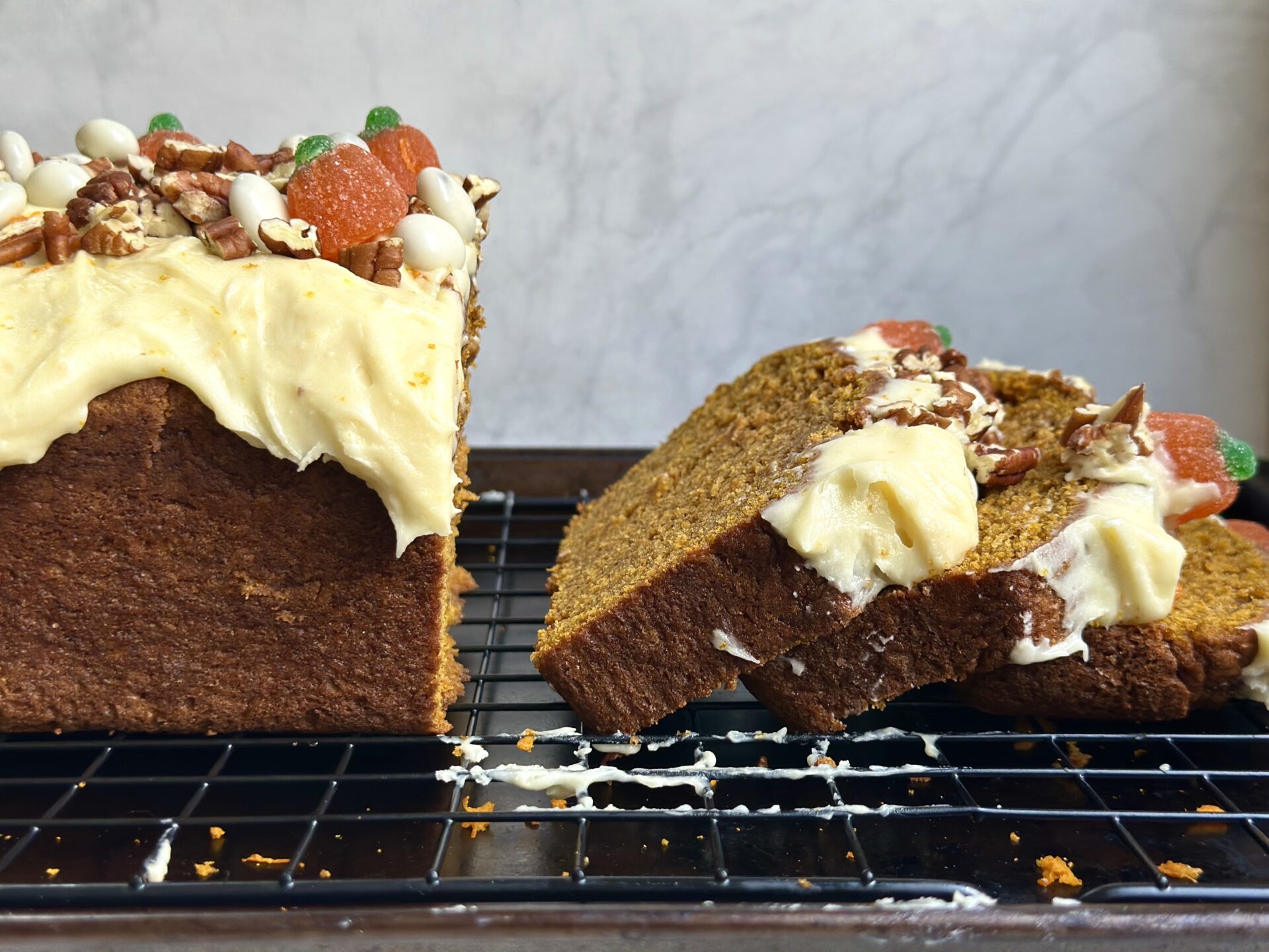 A loaf of pumpkin bread with orange cream cheese frosting is sliced and seen from the side