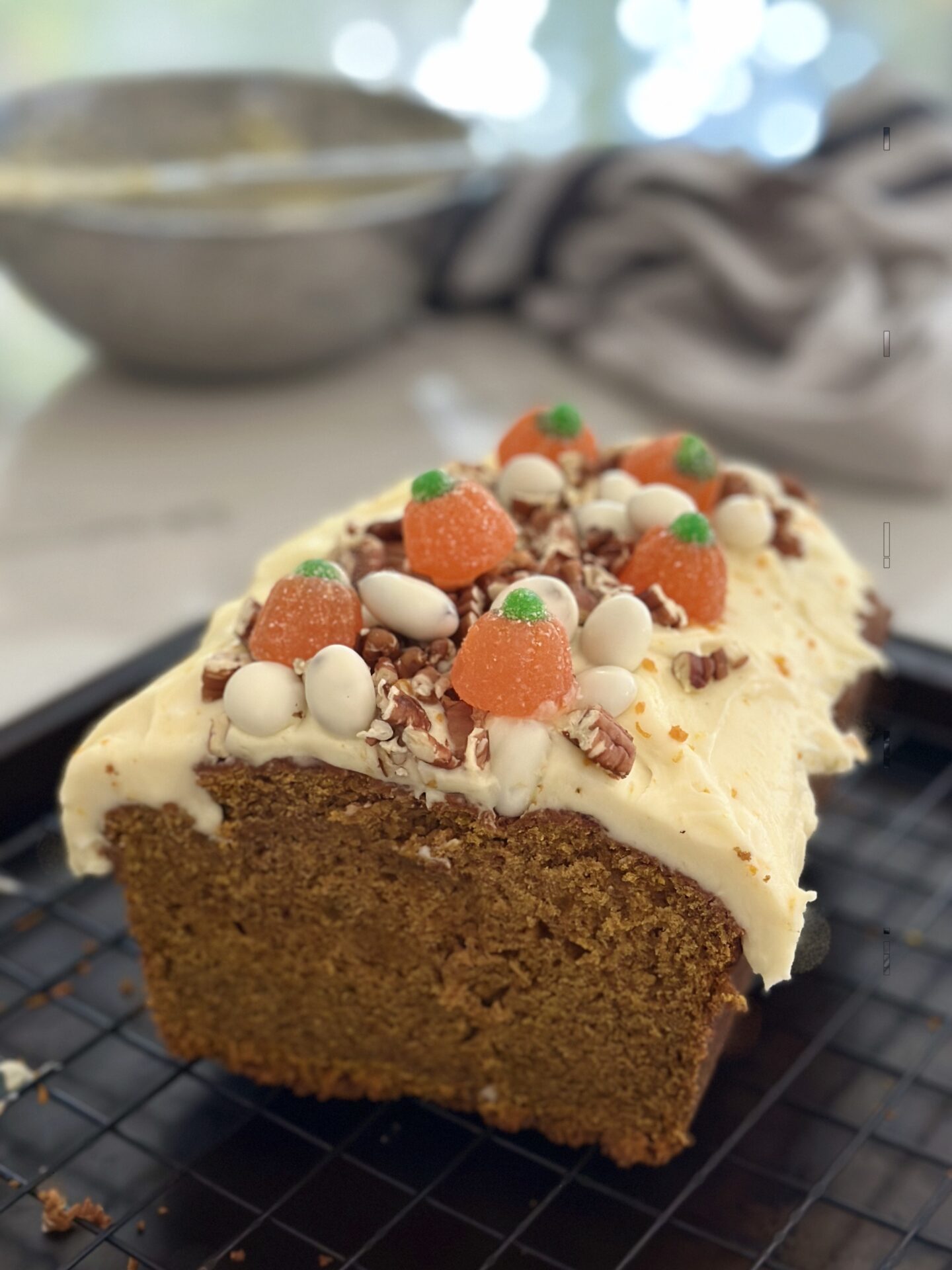 A loaf of pumpkin bread with orange cream cheese frosting is cut into, revealing the tender moist interior