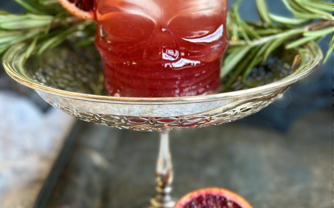 A blood orange and black currant aperol spritz served in a halloween themed glass on a silver tray