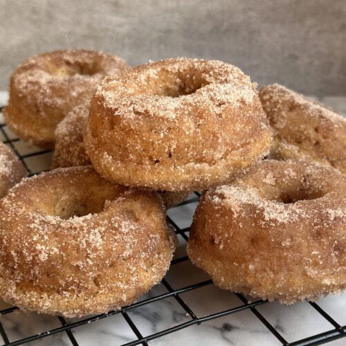 Freshly baked Cinnamon Sugar Donuts are stacked high on a cooling rack