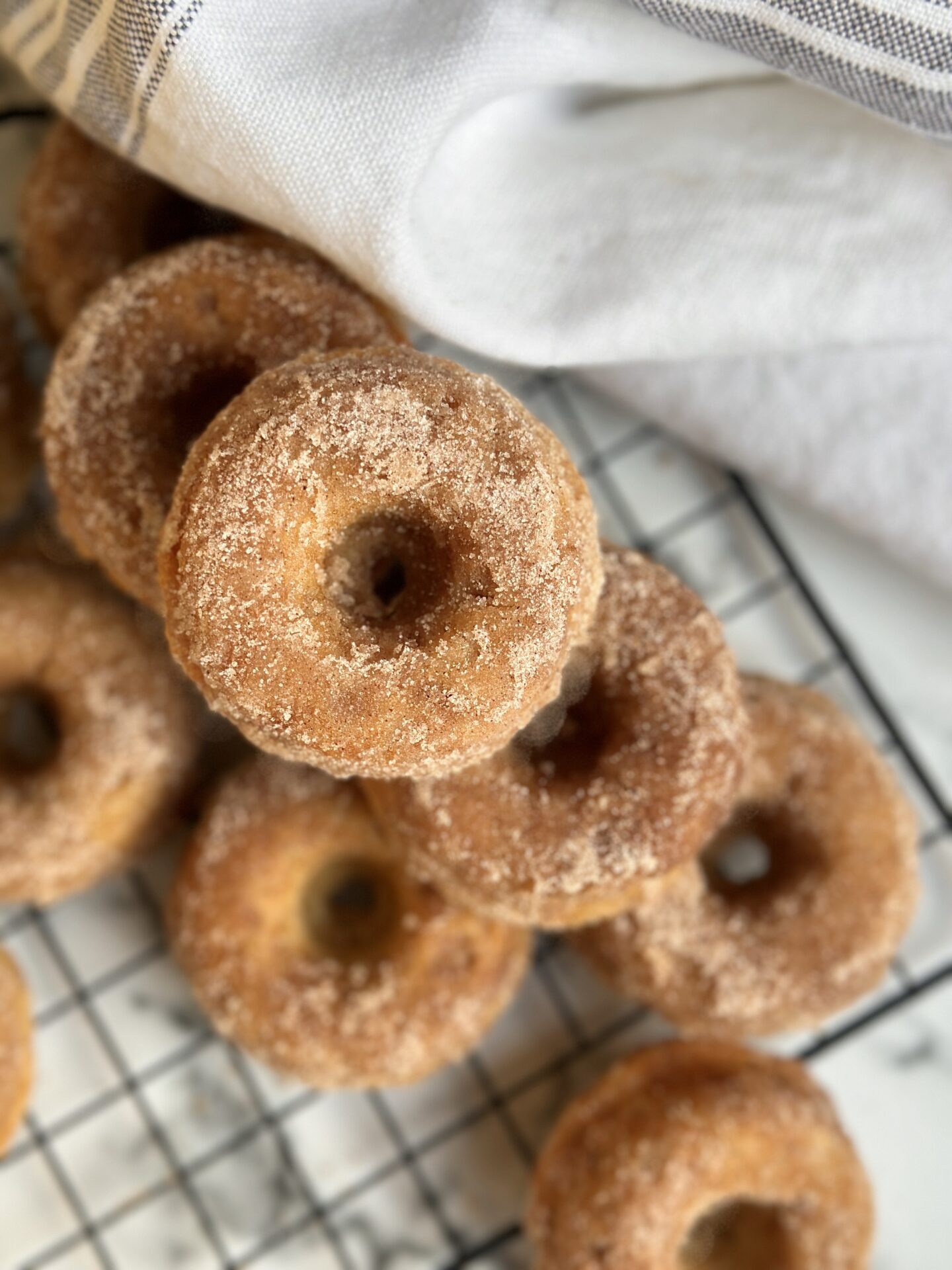 A stack of freshly baked Cinnamon Sugar donuts on a black wire cooling rack is seen from above