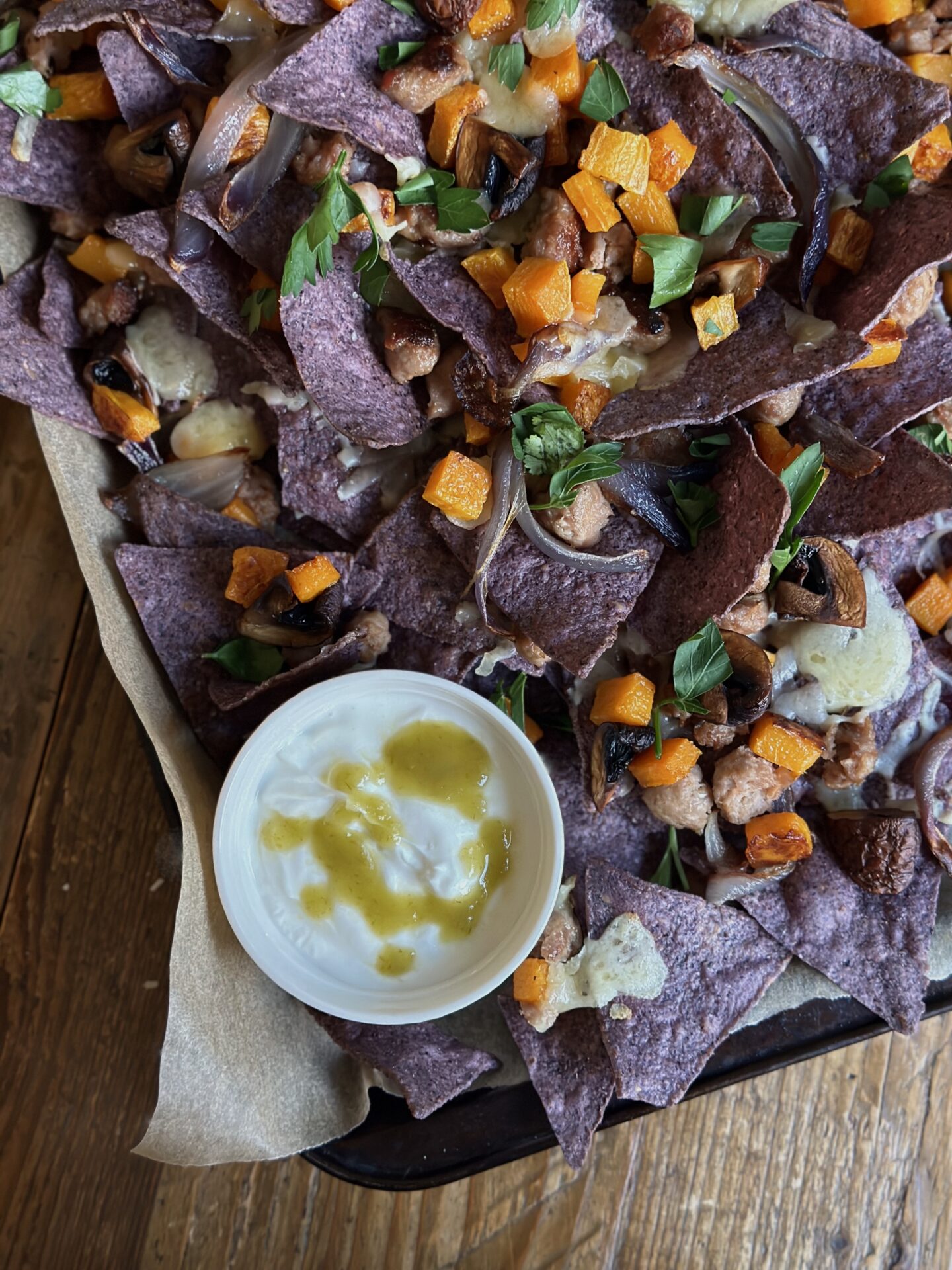 A tray of homemade blue corn harvest nachos is seen from above with a dish of jalapeño drizzled sour cream