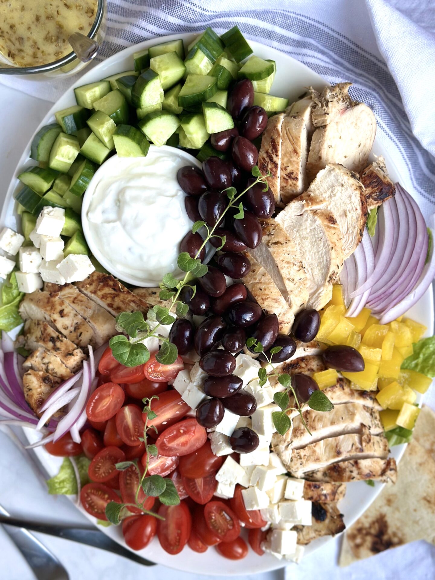 A large platter of Grilled Chicken Greek Salad is seen from above with generous amounts of tomatoes, cucumber, chicken, feta cheese and olives
