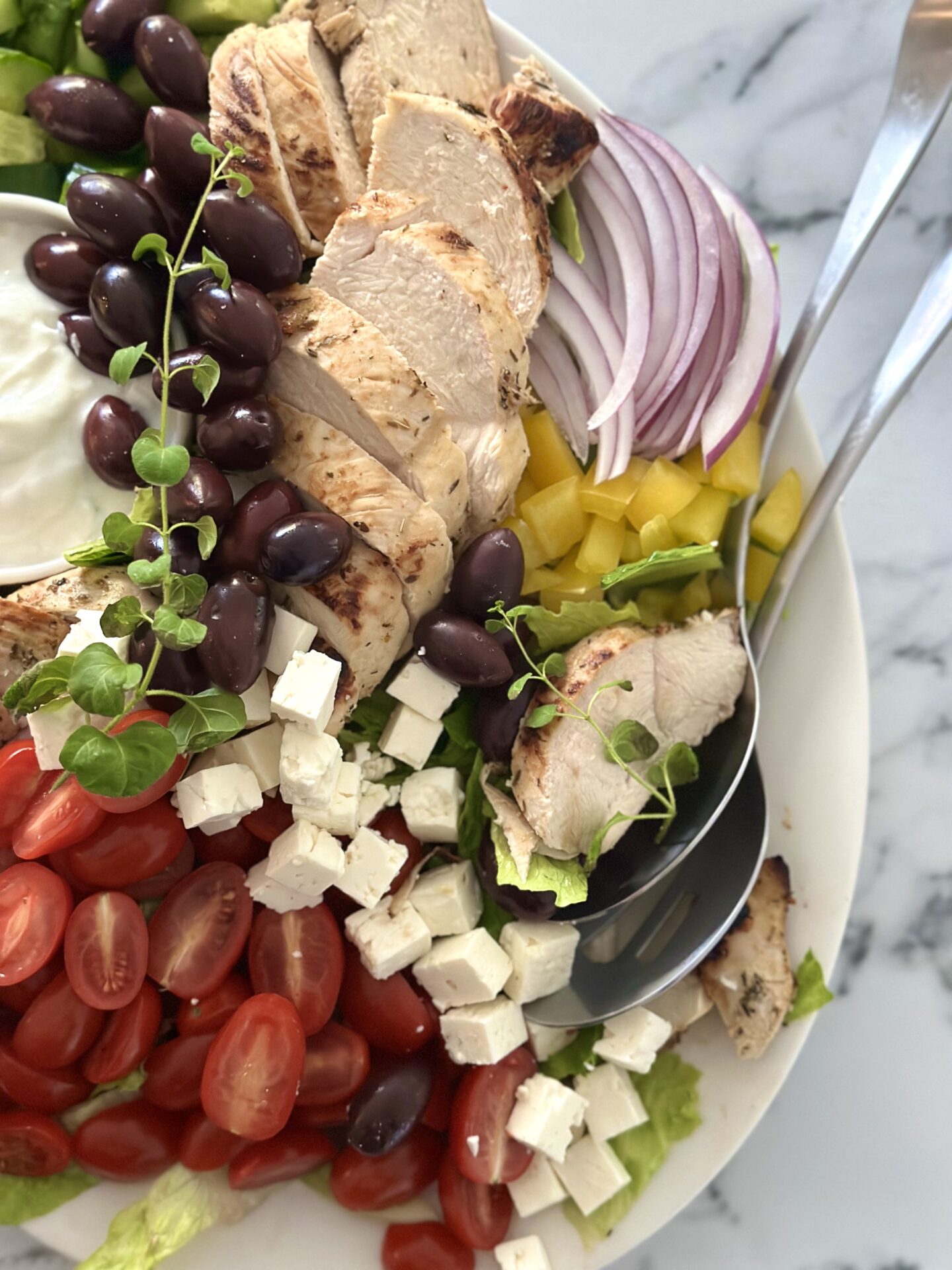 Serving spoons are placed on the edge of a big platter of Grilled Chicken Souvlaki Salad