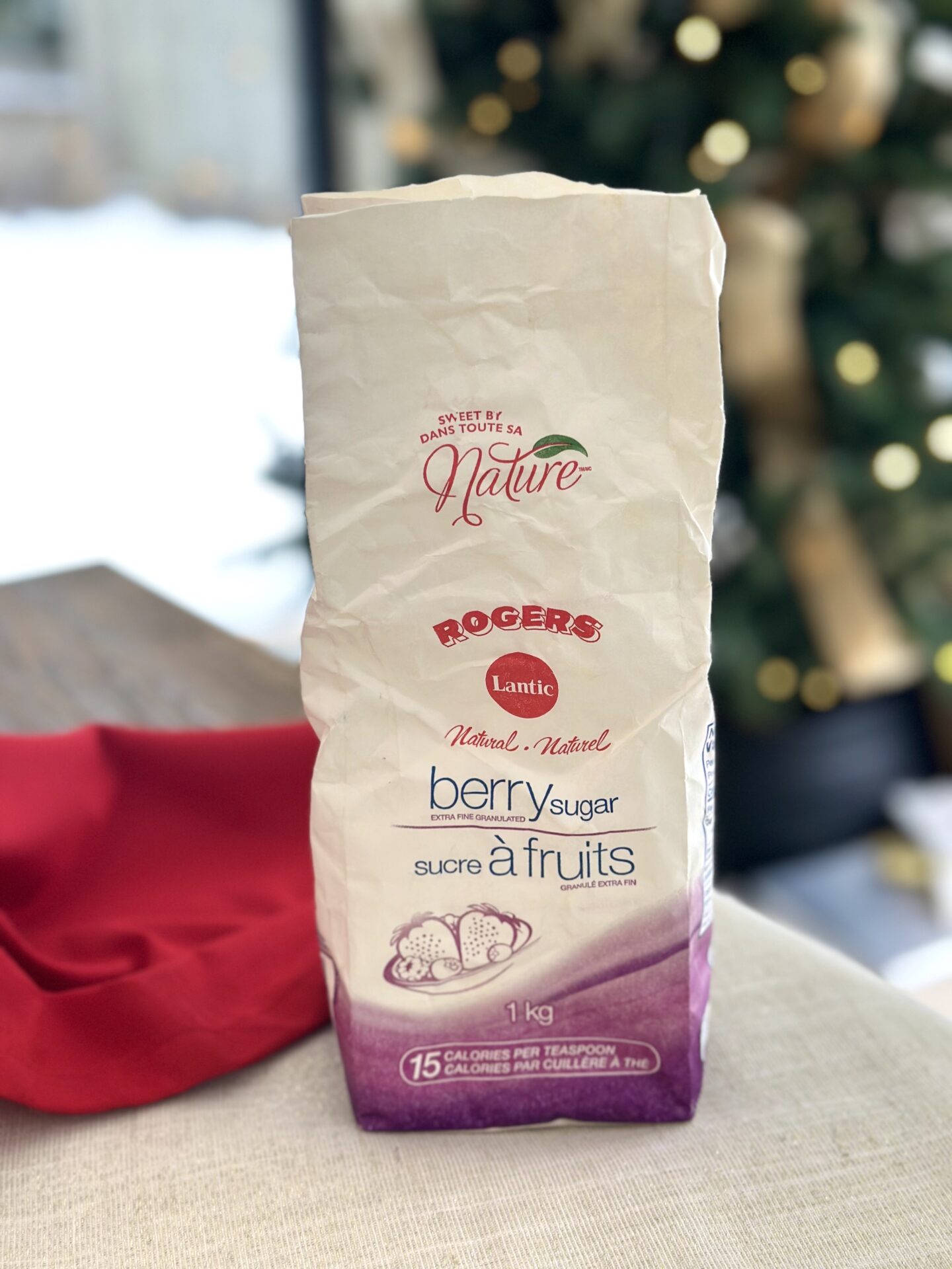 A bag of berry sugar is seen on a marble table in front of a Christmas tree