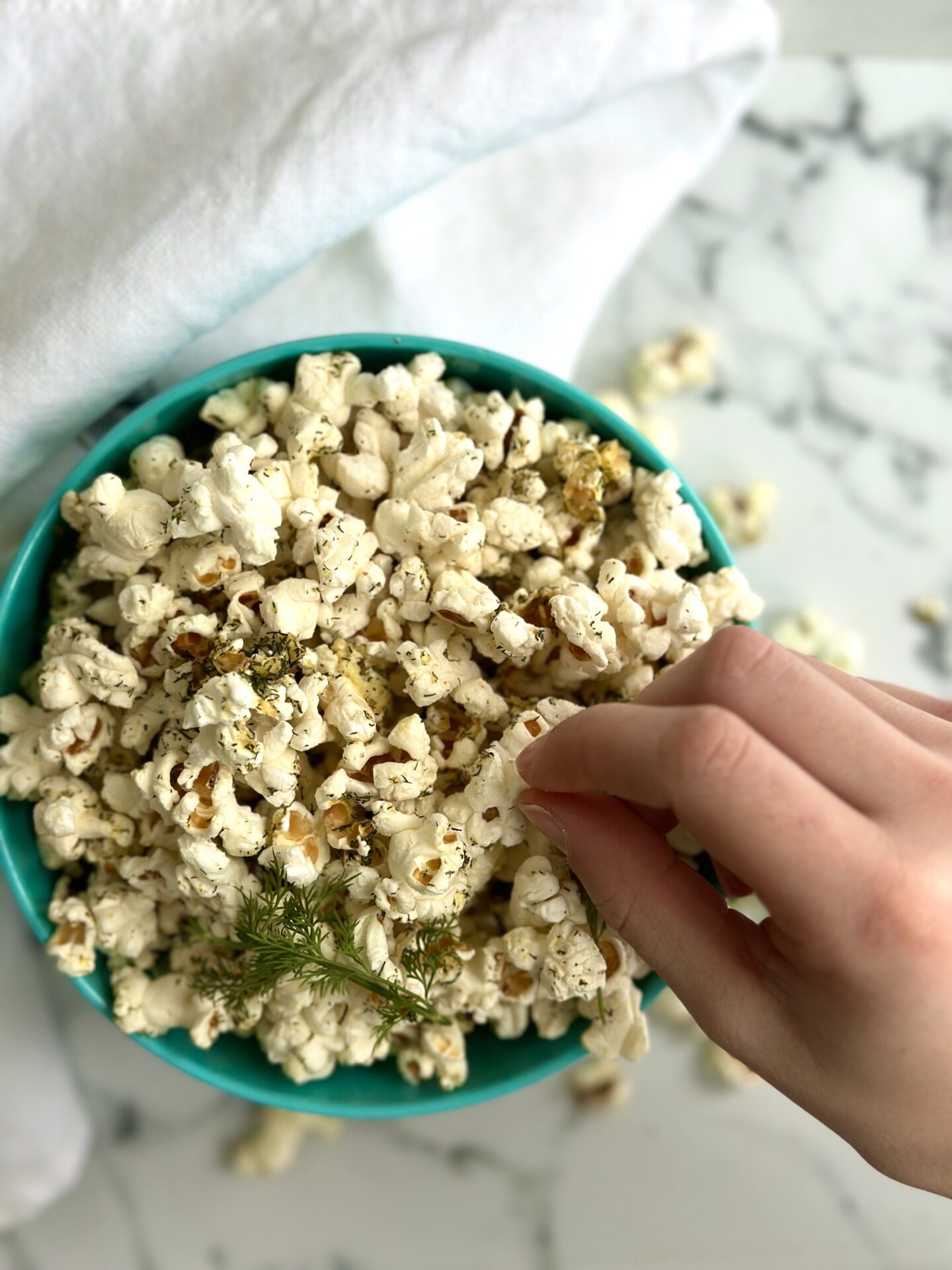 A bowl of dill pickle popcorn is seen from above with a small hand reaching in to grab a piece