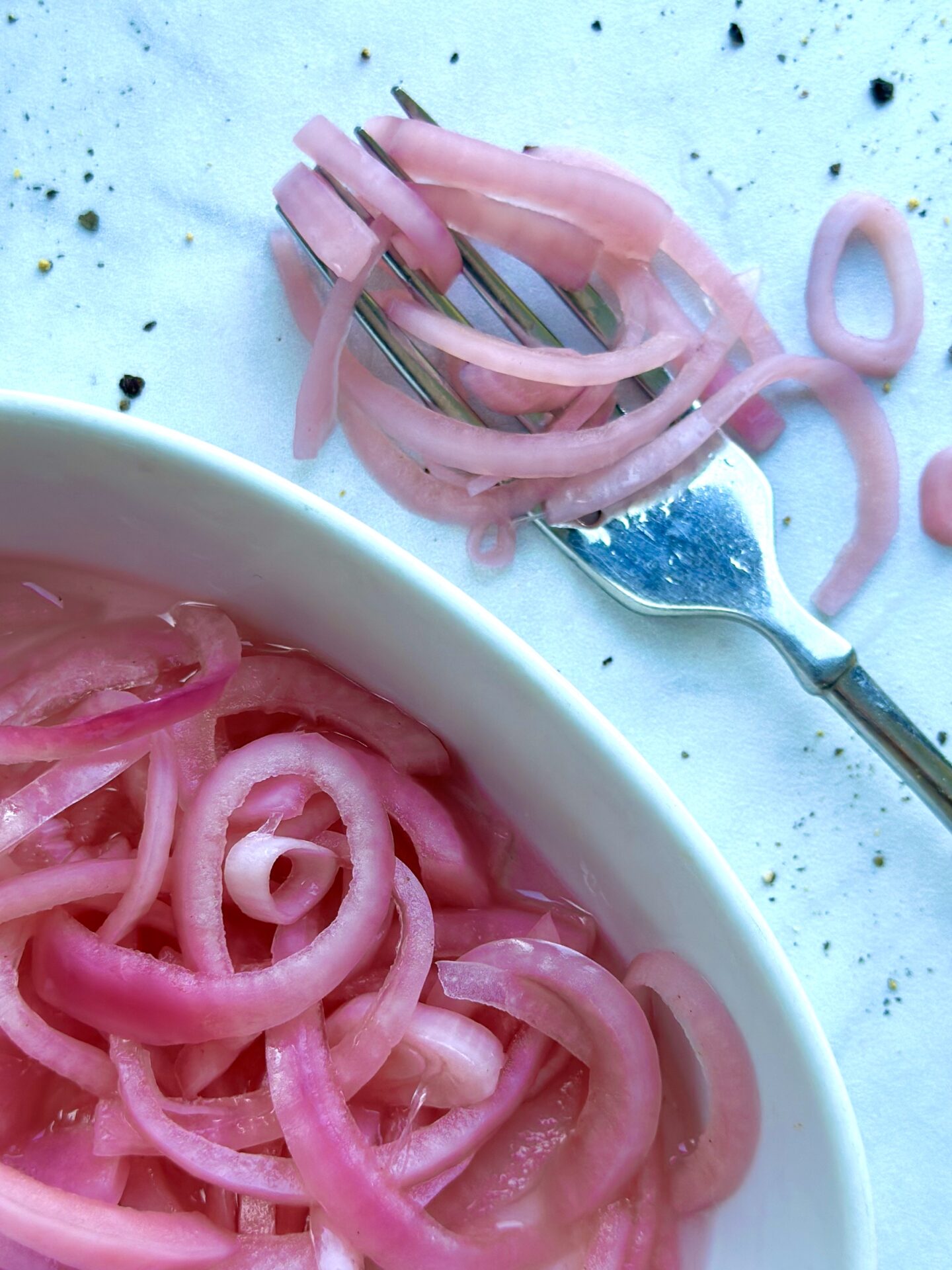 A dish of bright pink pickled red onions is seen from above with a fork