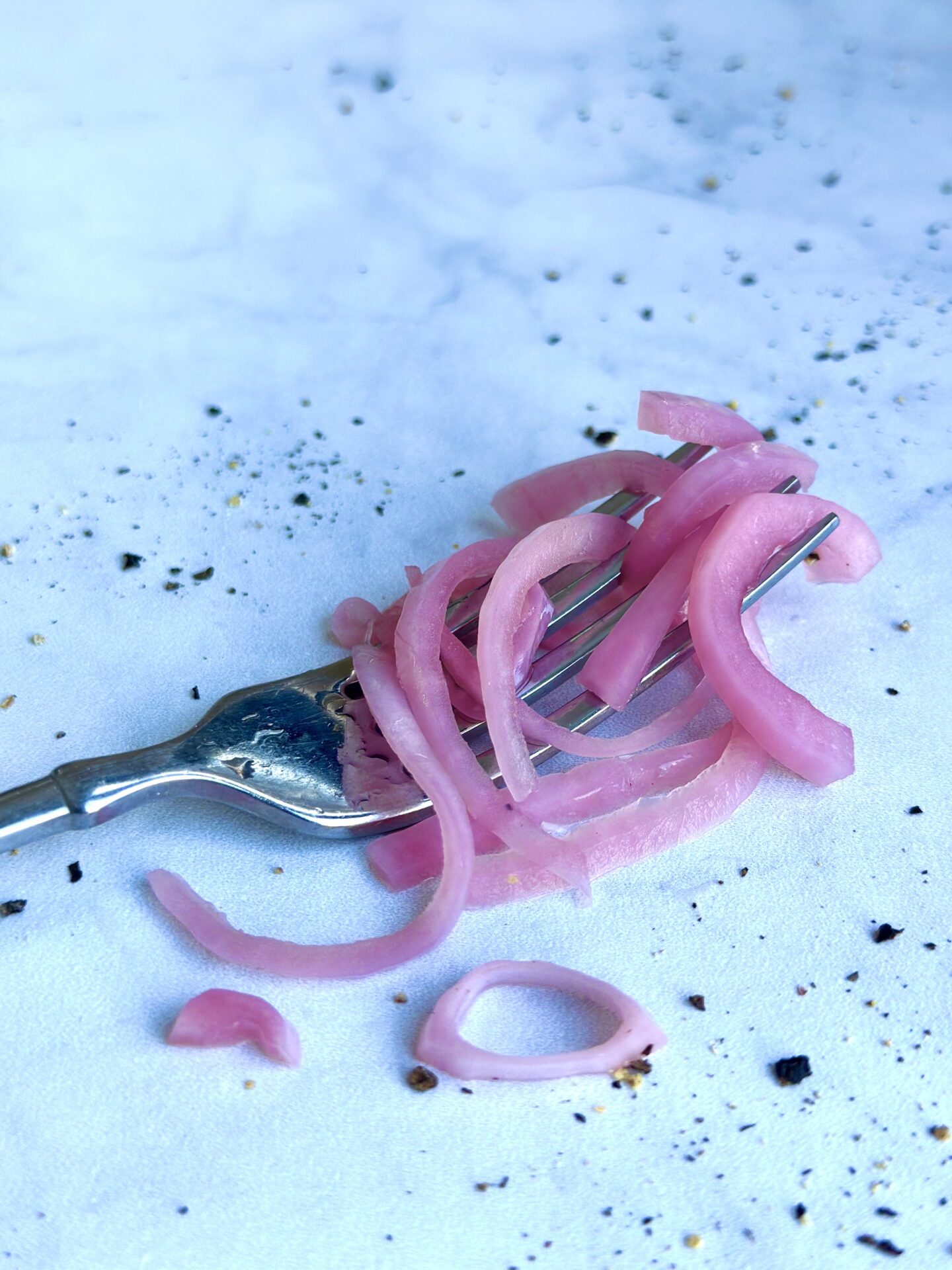 A forkful of tangled bright pink pickled red onions sits on a white marble table