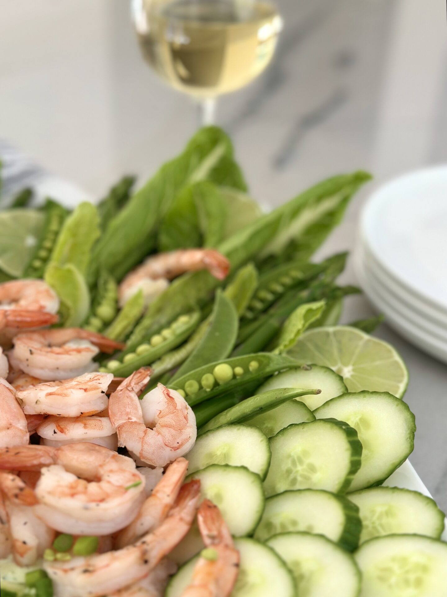 A platter of roasted shrimp and spring vegetables with creamy herb dip is seen with a chilled glass of white wine