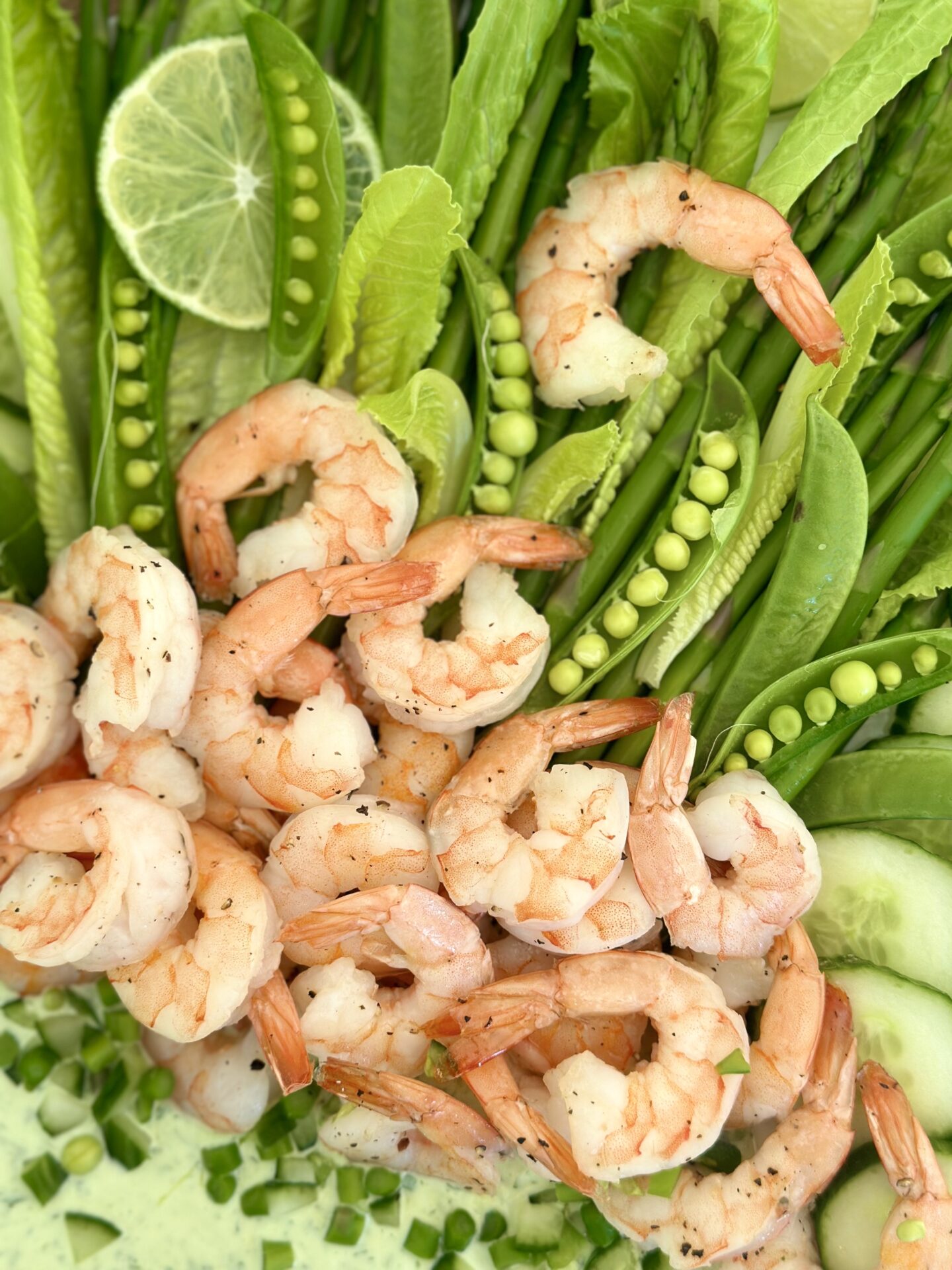 An artfully arranged platter of roasted shrimp and spring vegetables with creamy herb dip is seen from above