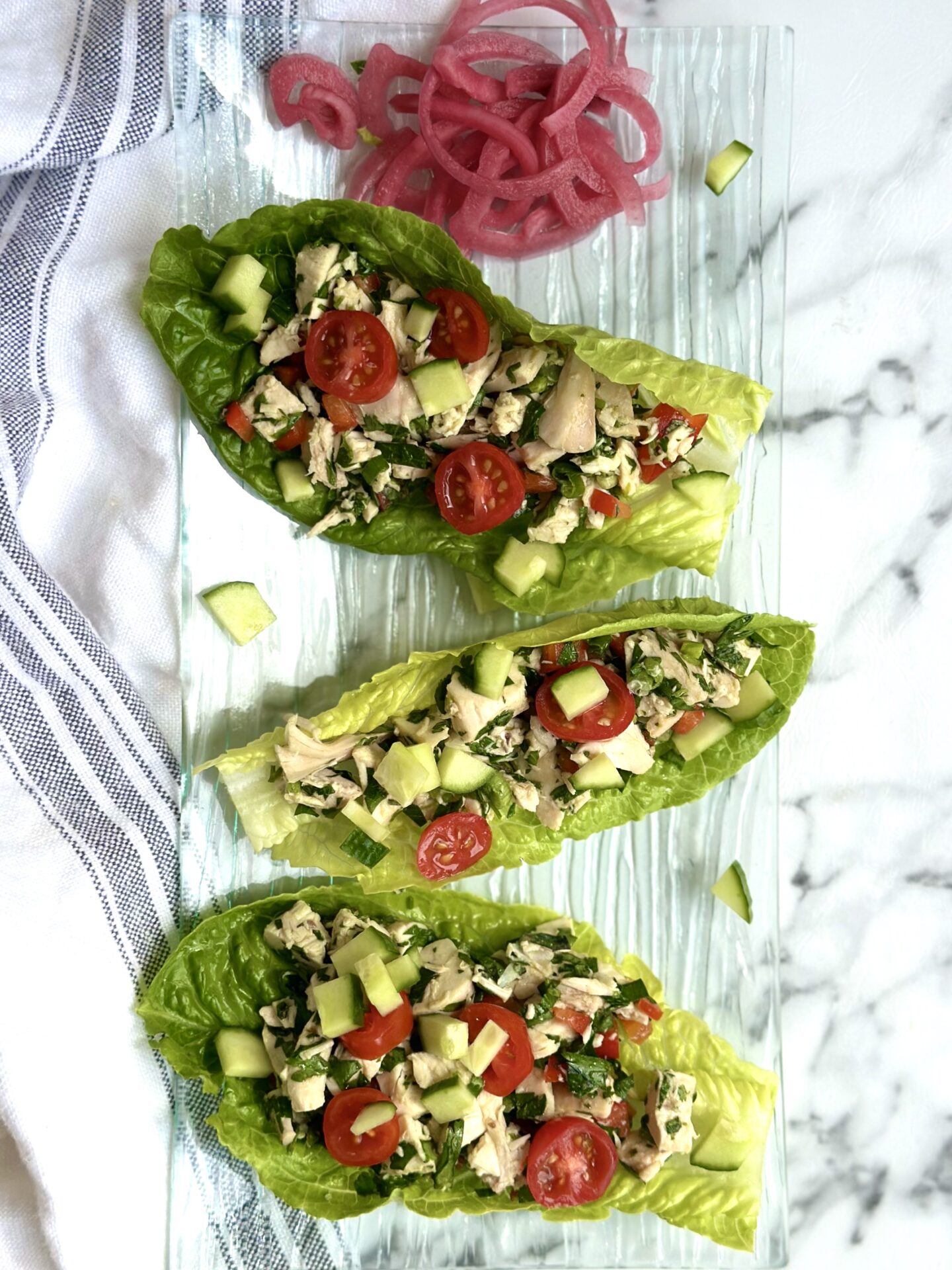 A trio of romaine lettuce leaves are stuffed with chimichurri chicken salad and served on a glass plate