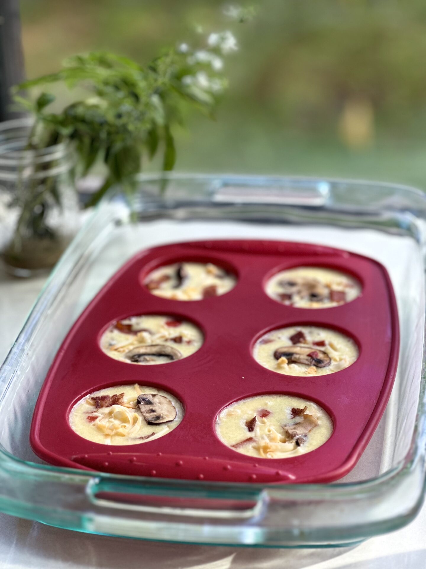 A silicone muffin mould filled with egg bite mixture is placed in a water bath to achieve a soft, custardy texture during baking