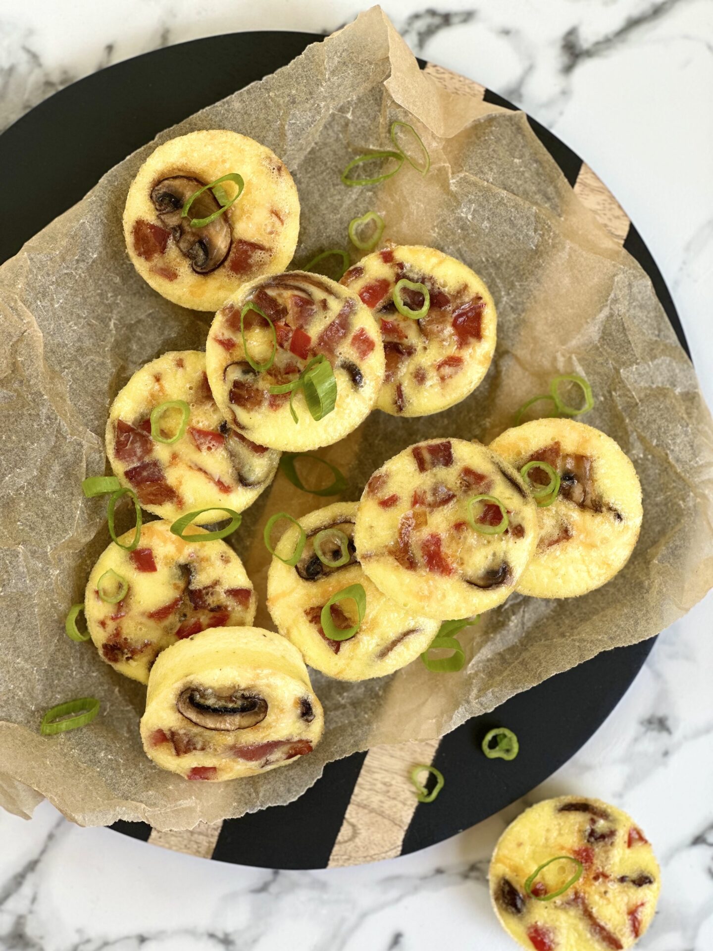 A platter of stacked oven baked egg bites with bacon, mushroom and pepper is seen from above on a white marble counter top