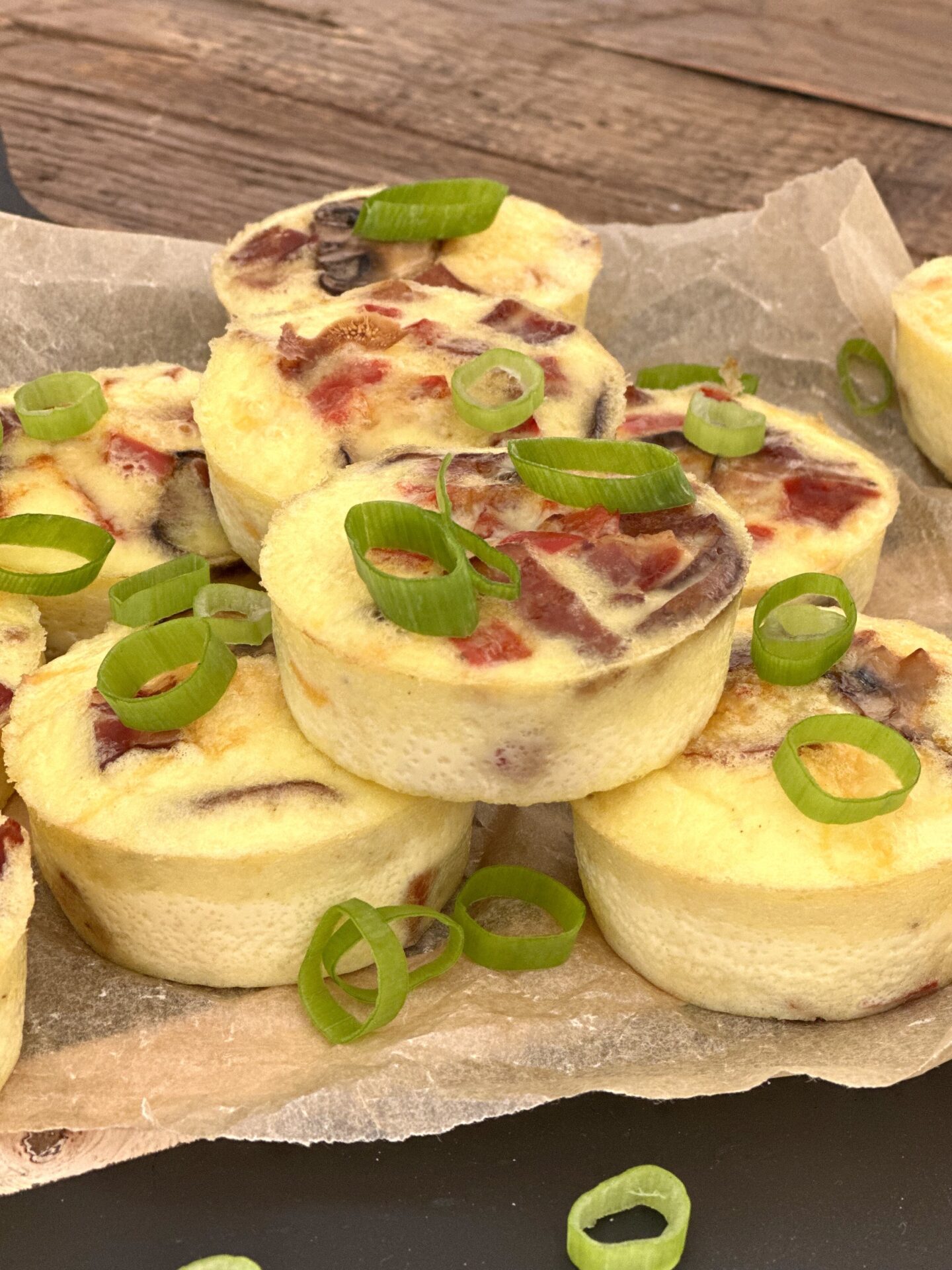 Oven baked egg bites with bacon, mushroom and peppers are seen from the side, stacked on  a parchment lined serving platter