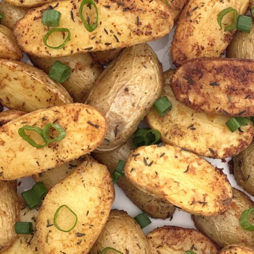 Golden roasted fingerling potatoes are seen in close up from above, garnished with chopped green onions