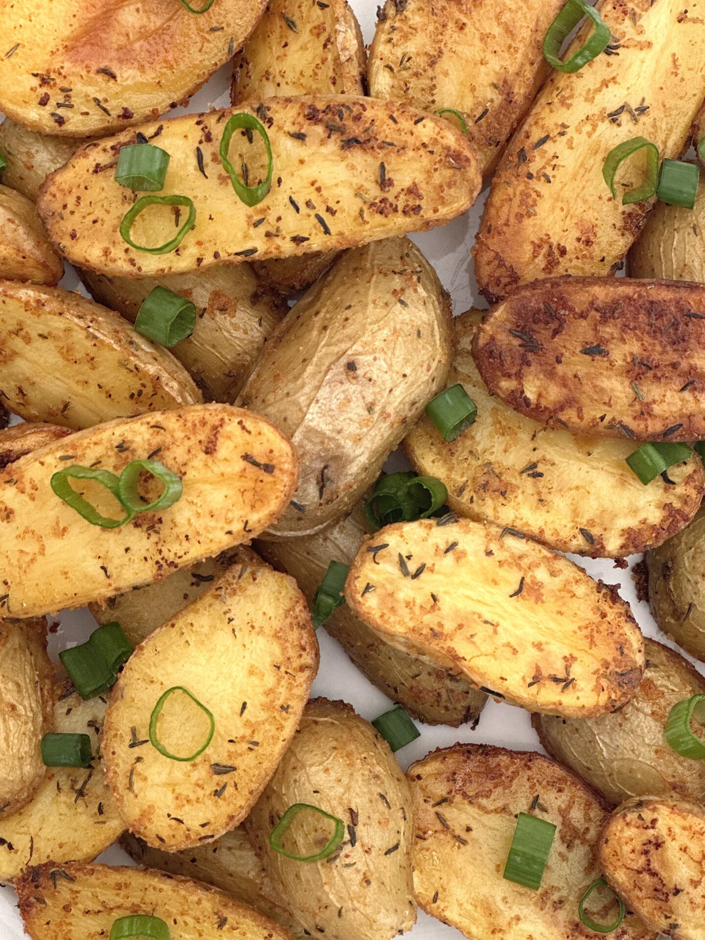 Golden roasted fingerling potatoes are seen in close up from above, garnished with chopped green onions