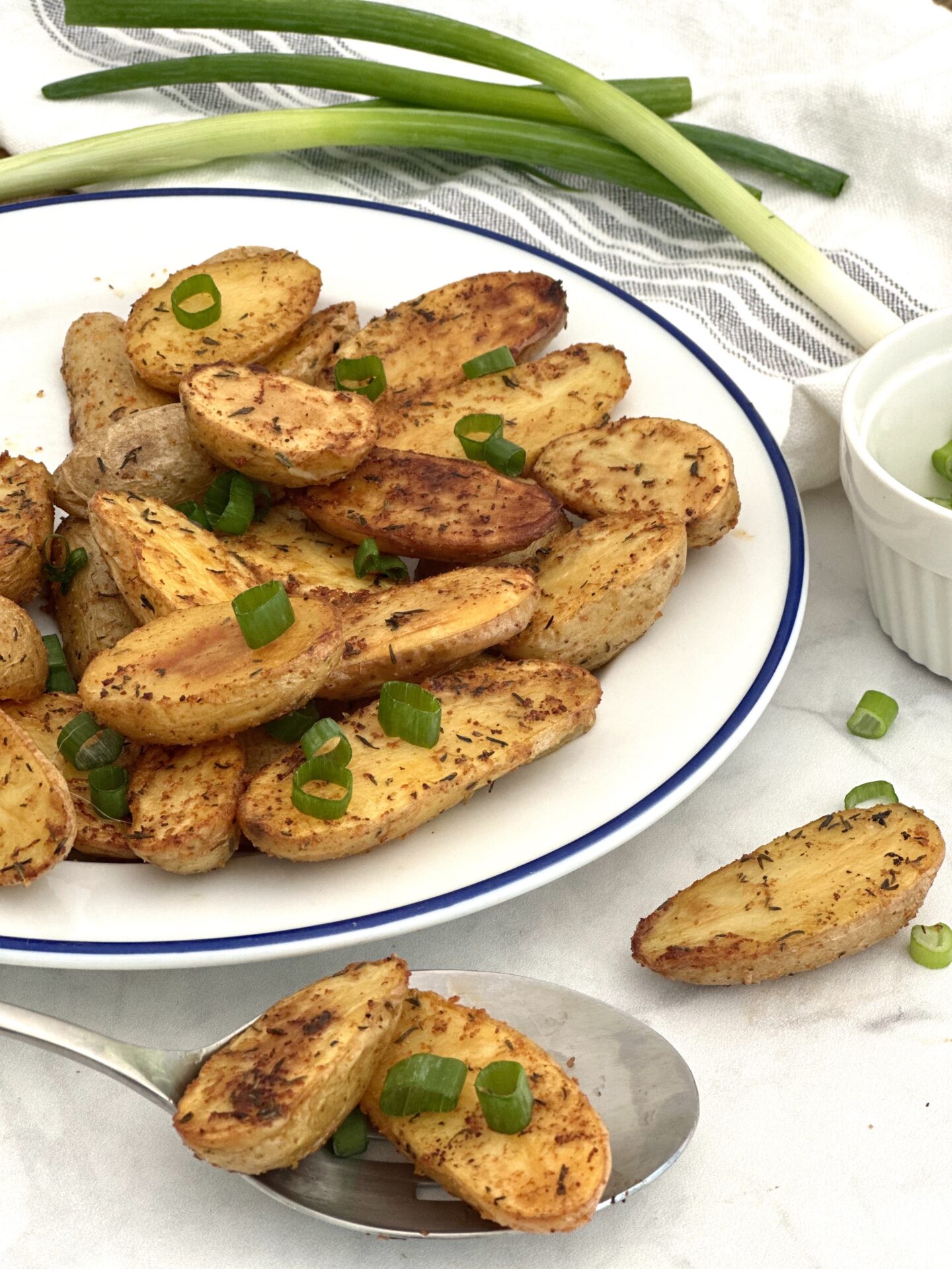 A platter of golden roasted fingerling potatoes overflows onto a white marble counter top