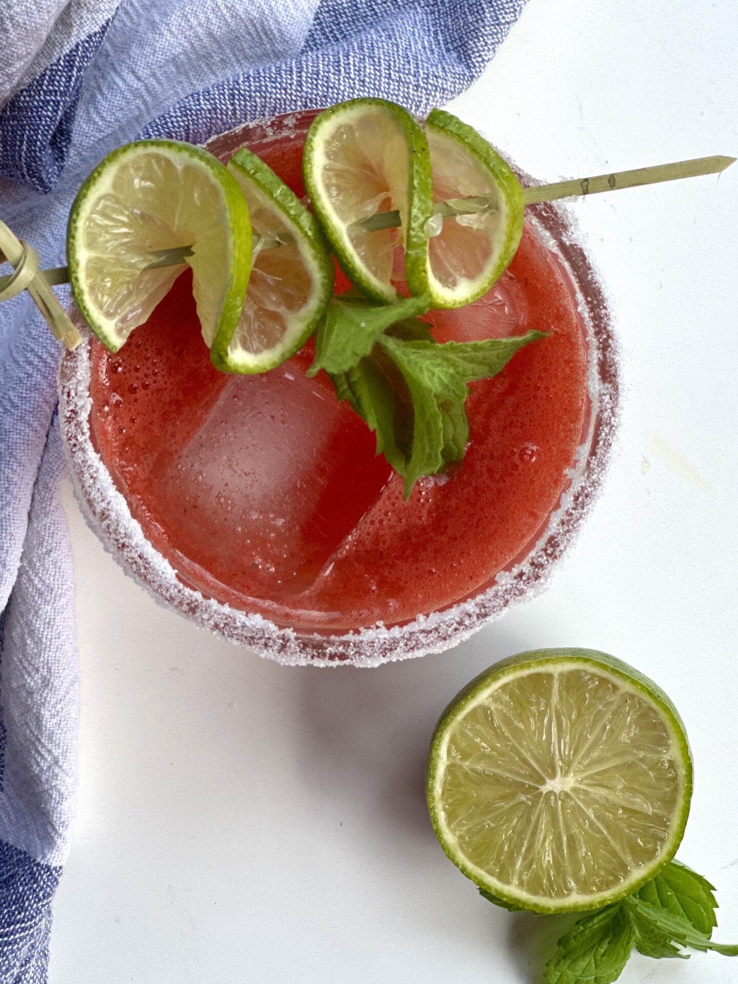 A sugar rimmed glass of watermelon agua fresca is seen from above, garnished with lime and mint