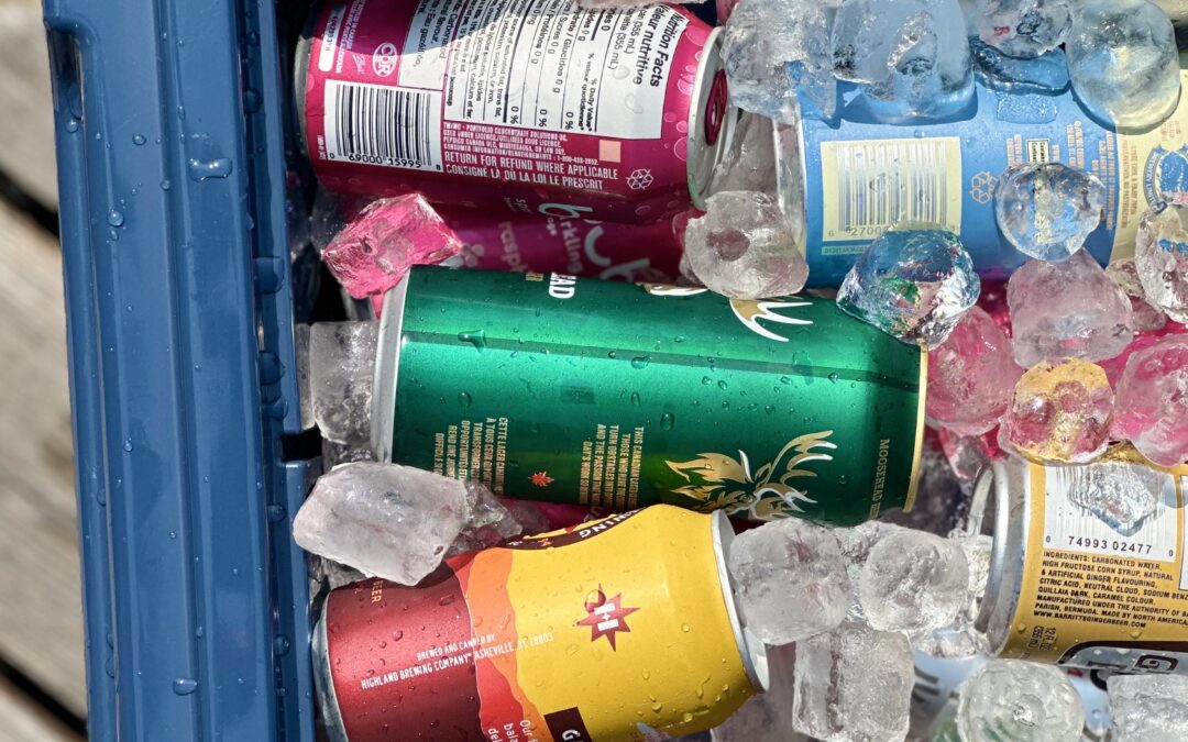 A well packed, sun lit cooler filled with ice, cans and bottles is seen from above, sitting on a wood dock