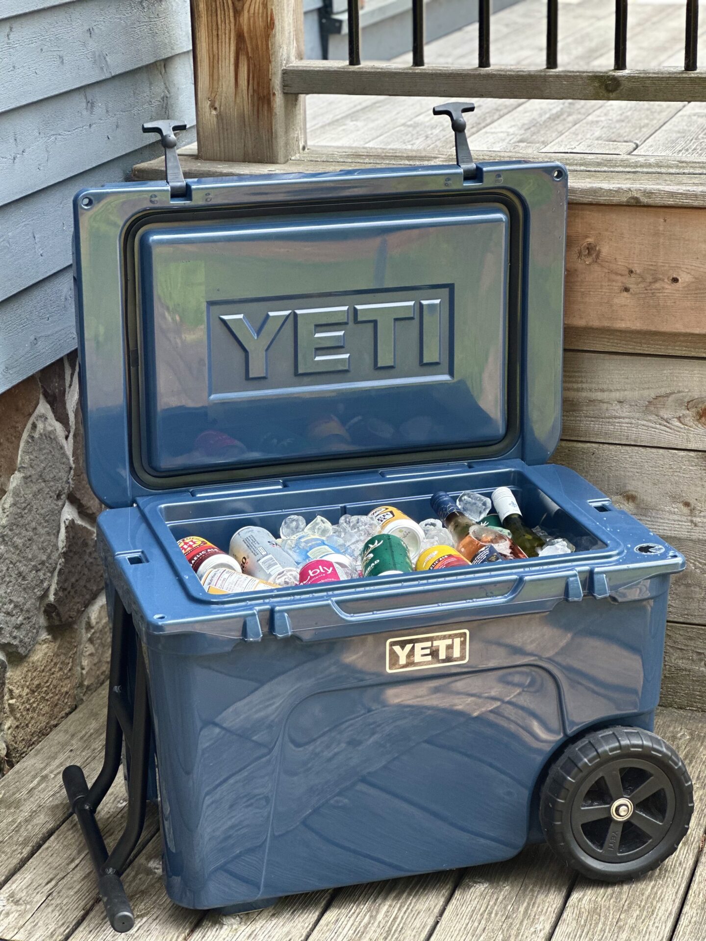 A dark blue Yeti cooler filled with ice and drinks sits open on a sunny deck