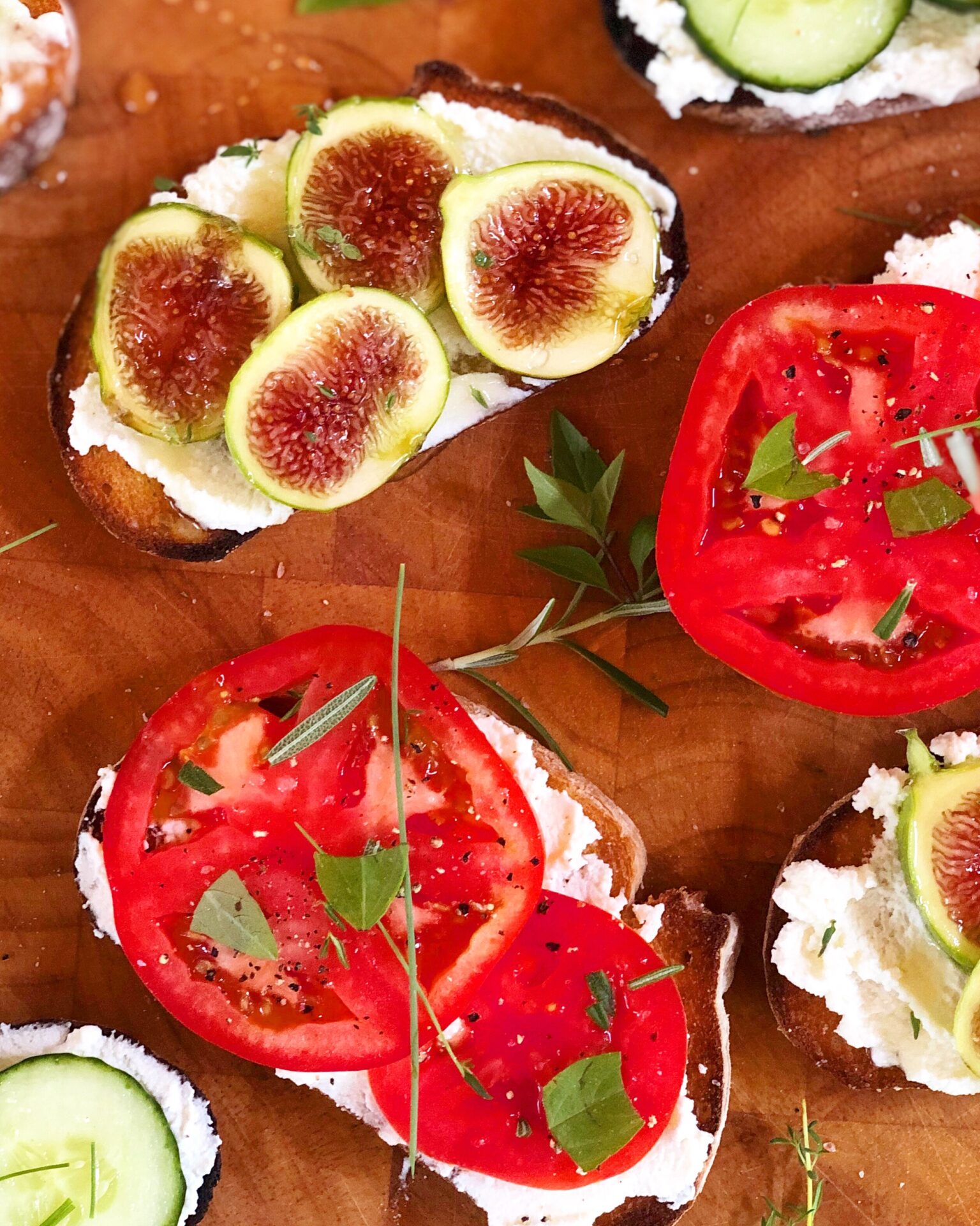 Open faced sandwiches are seen from above, slathered with homemade ricotta cheese and some topped with fresh tomatoes and herbs, and some topped with fresh fig slices and honey.