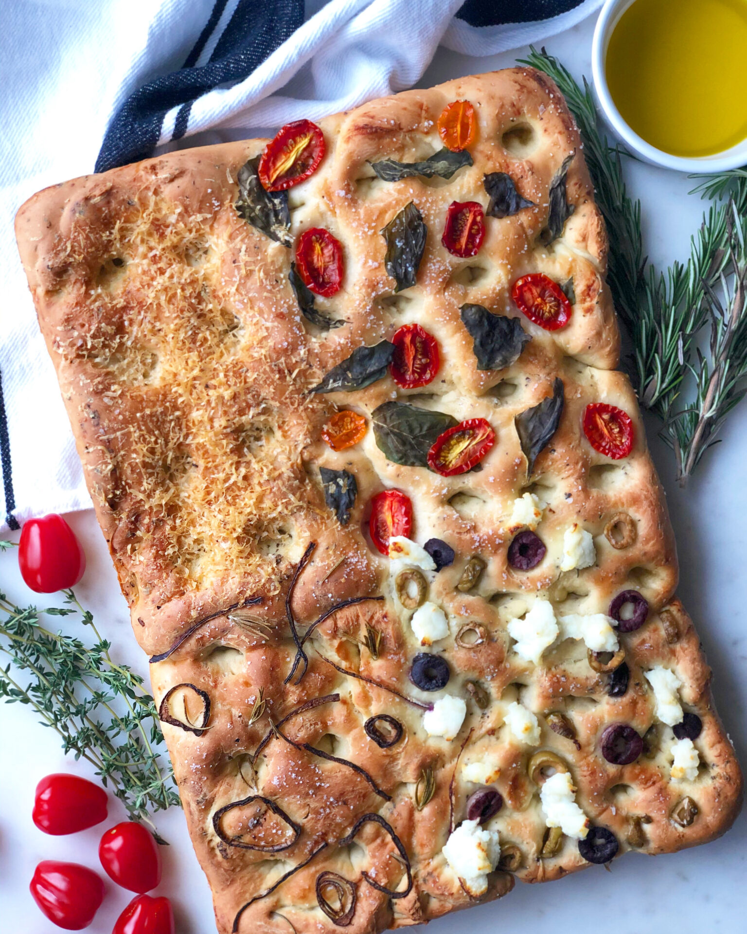 A rectangular focaccia bread is divided into 4 sections, each section topped with a different selection of vegetables, meats and cheeses