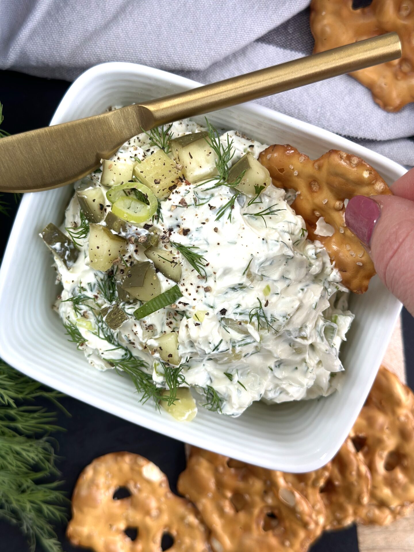 A hand is seen dipping a pretzel chip into homemade Dill Pickle Dip