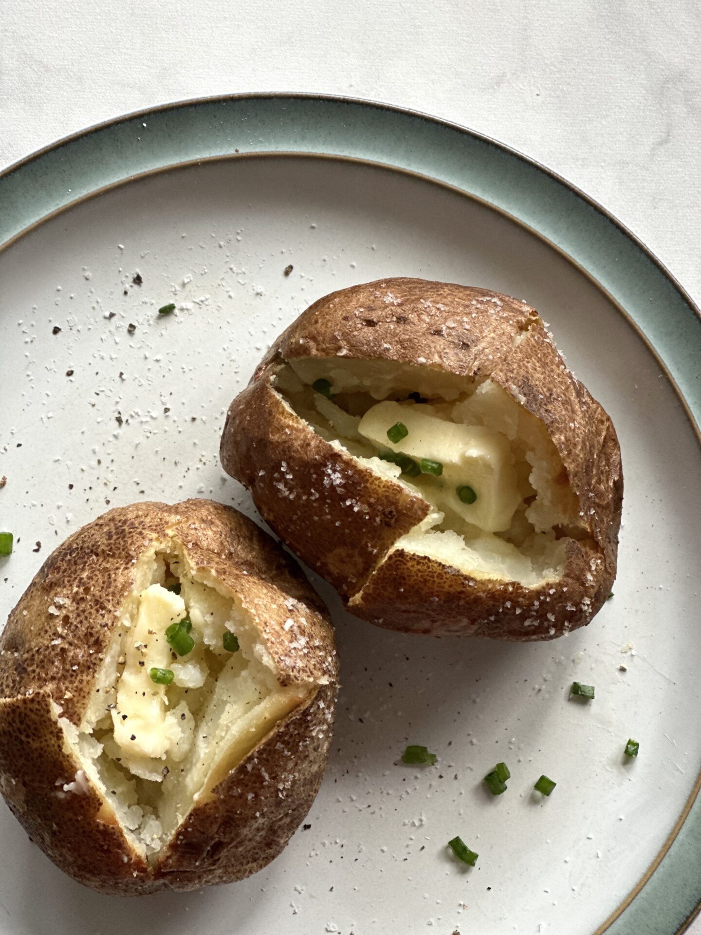 Perfect, crispy skinned baked potatoes and seen from above, split open and filled with a generous pat of butter and garnished with chopped chives.