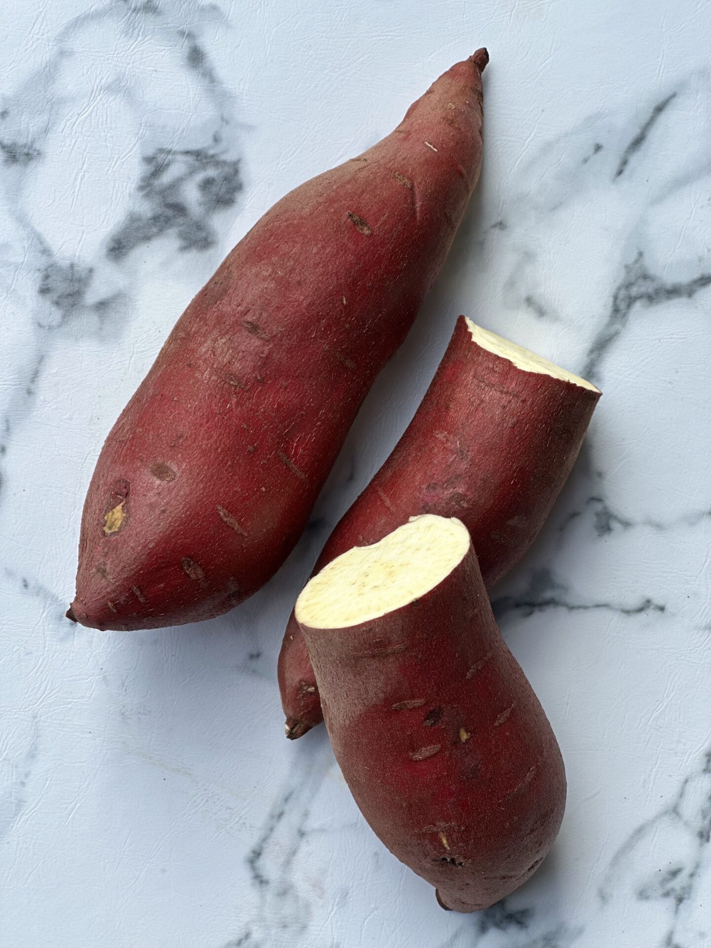 Two Japanese sweet potatoes are seen from above, one is whole and one is cut in half exposing the creamy interior