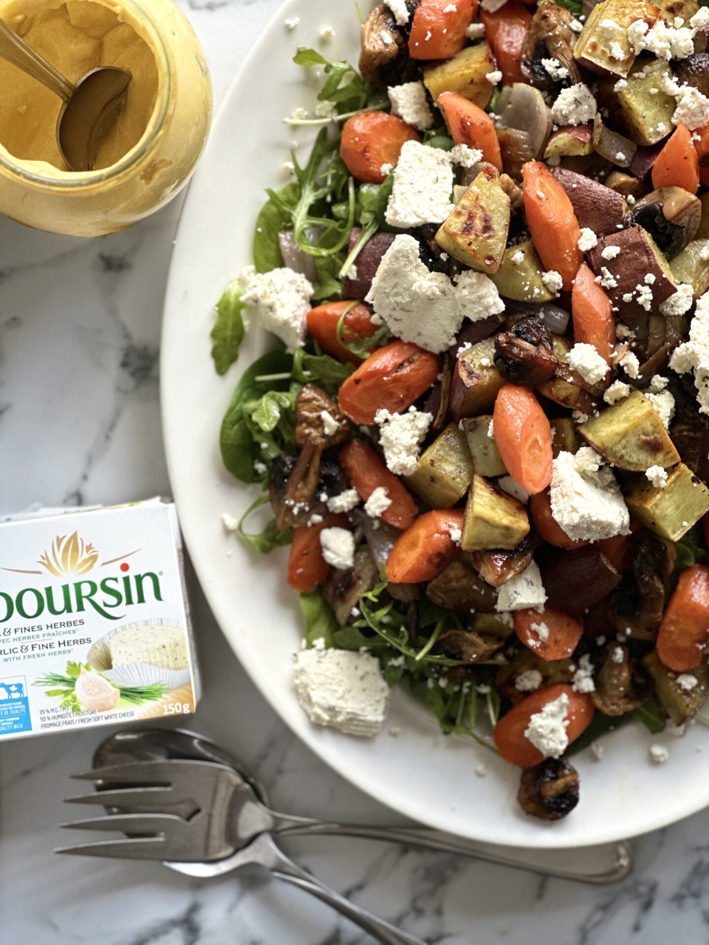 A platter of Warm Roasted Vegetable Salad with Boursin is seen from above, surrounded by a package of Boursin cheese and an open jar of dijon mustard.