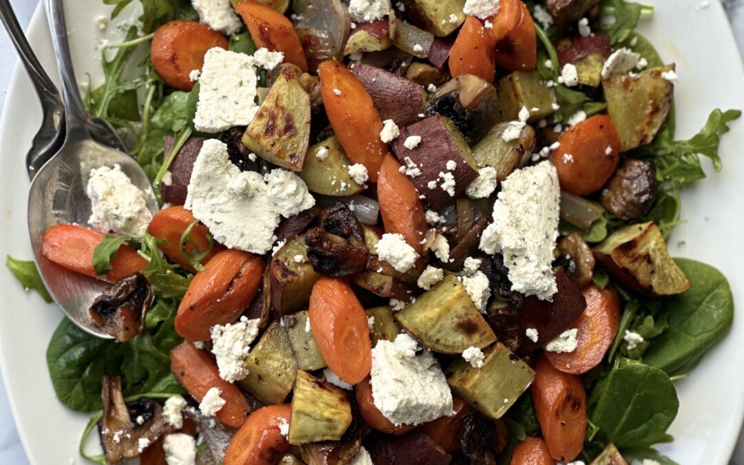 A large platter of Warm Roasted Vegetable and Boursin Salad is seen from above on a white marble table.