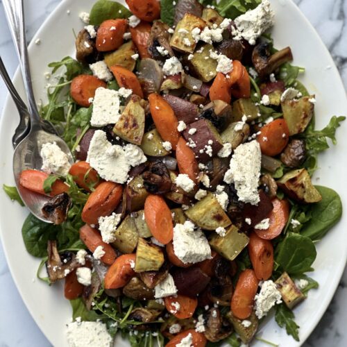 A large platter of Warm Roasted Vegetable and Boursin Salad is seen from above on a white marble table.