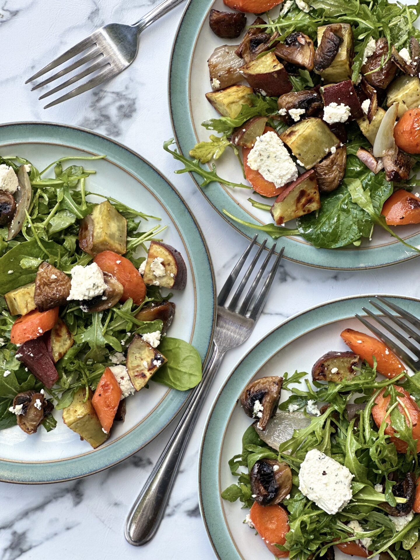 Three plates filled with servings of Warm Roasted Vegetable and Boursin Salad are seen from above and surrounded by forks.