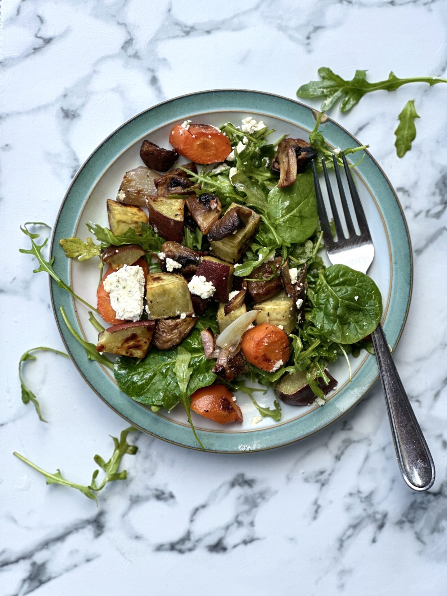 A single plate of Warm Roasted Vegetable and Boursin Salad is seen from above, overflowing onto a white marble tabletop