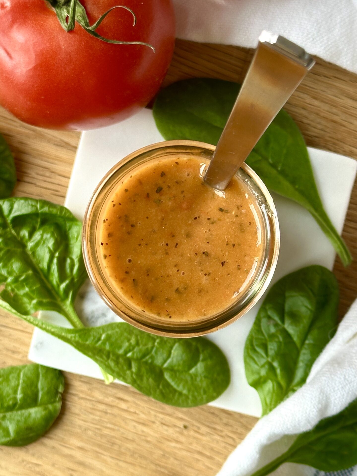 A glass jar of Sundried Tomato Vinaigrette is seen from above, surrounded by bright red tomatoes and salad greens