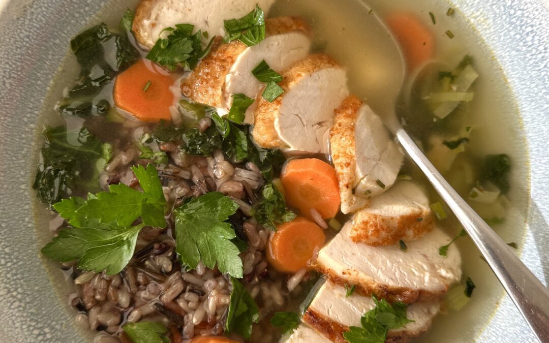 A bowl of Turkey, Leek and Wild Rice Soup is seen from above, garnished with large slices of juicy turkey and fresh parsley