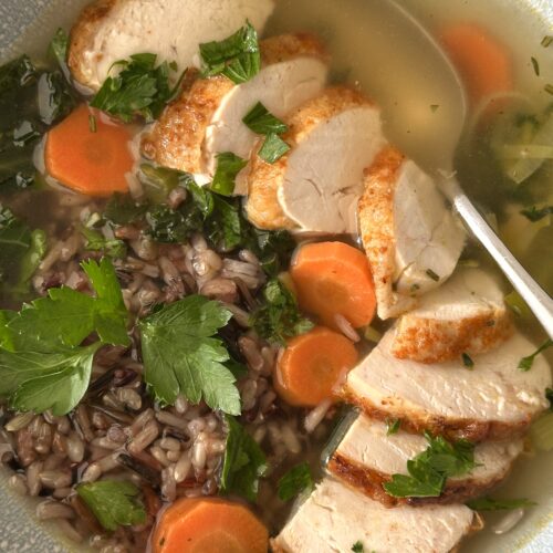 A bowl of turkey leek and wild rice soup is seen in close up, from above, with large slices of juicy turkey and a heap of wild rice nestled in a golden broth.