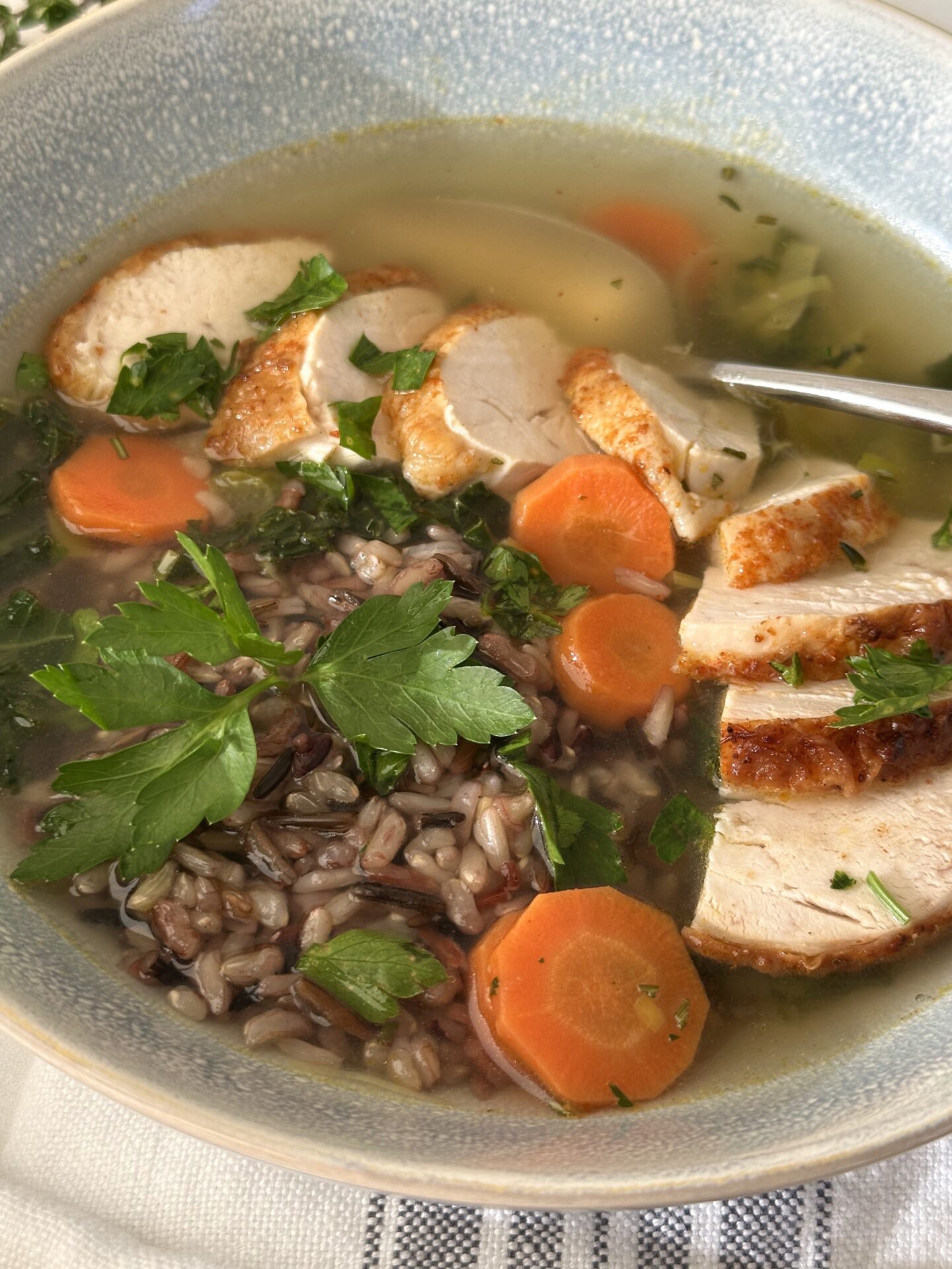 A bowl of turkey, leek and wild rice soup is seen close up, garnished with fresh parsley