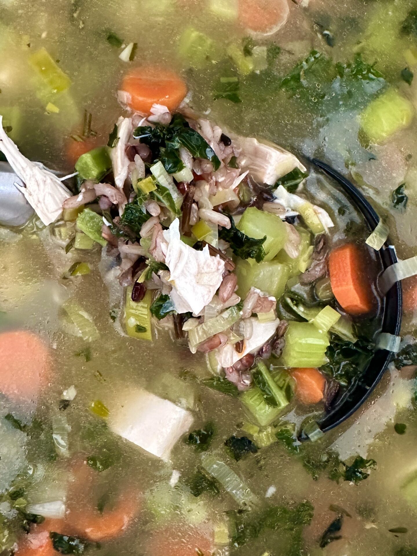 A ladle full of turkey, leek and wild rice soup is seen from above, hovering above a simmering pot of the soup